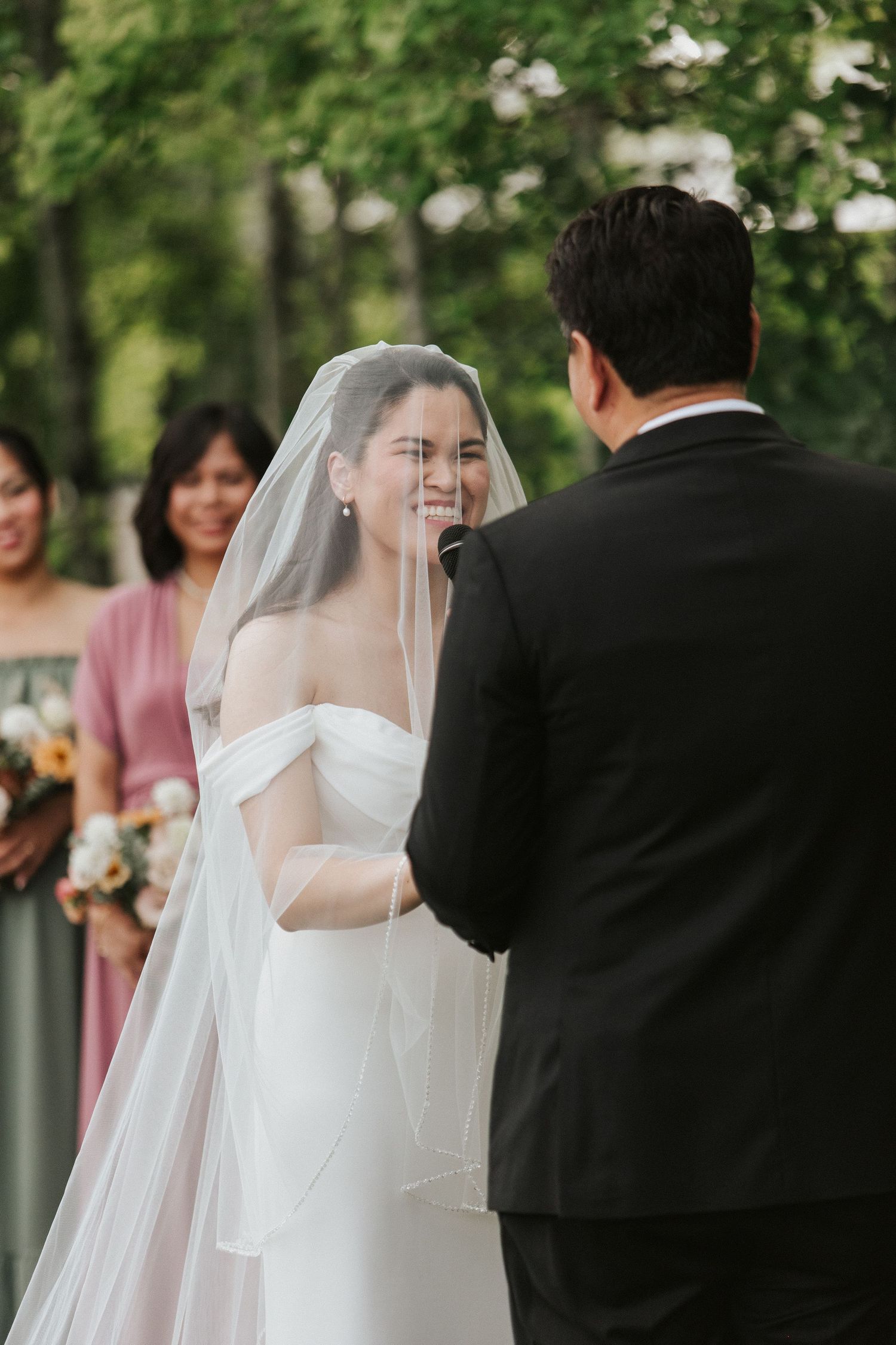 A joyful wedding ceremony moment with bridesmaids in pink dresses watching in the background.