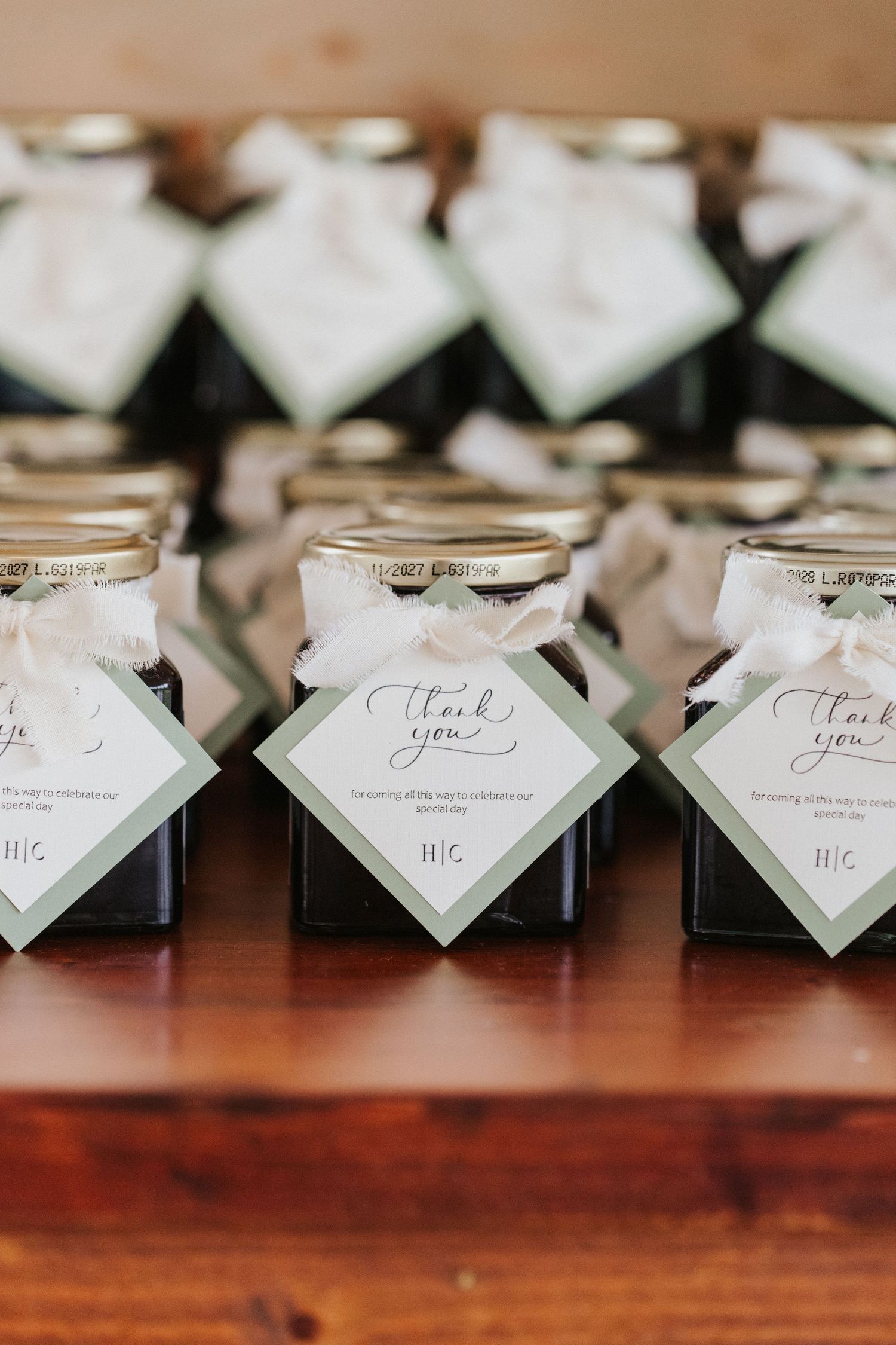 Small mason jars with thank you tags lined up as wedding favors on a wooden table.