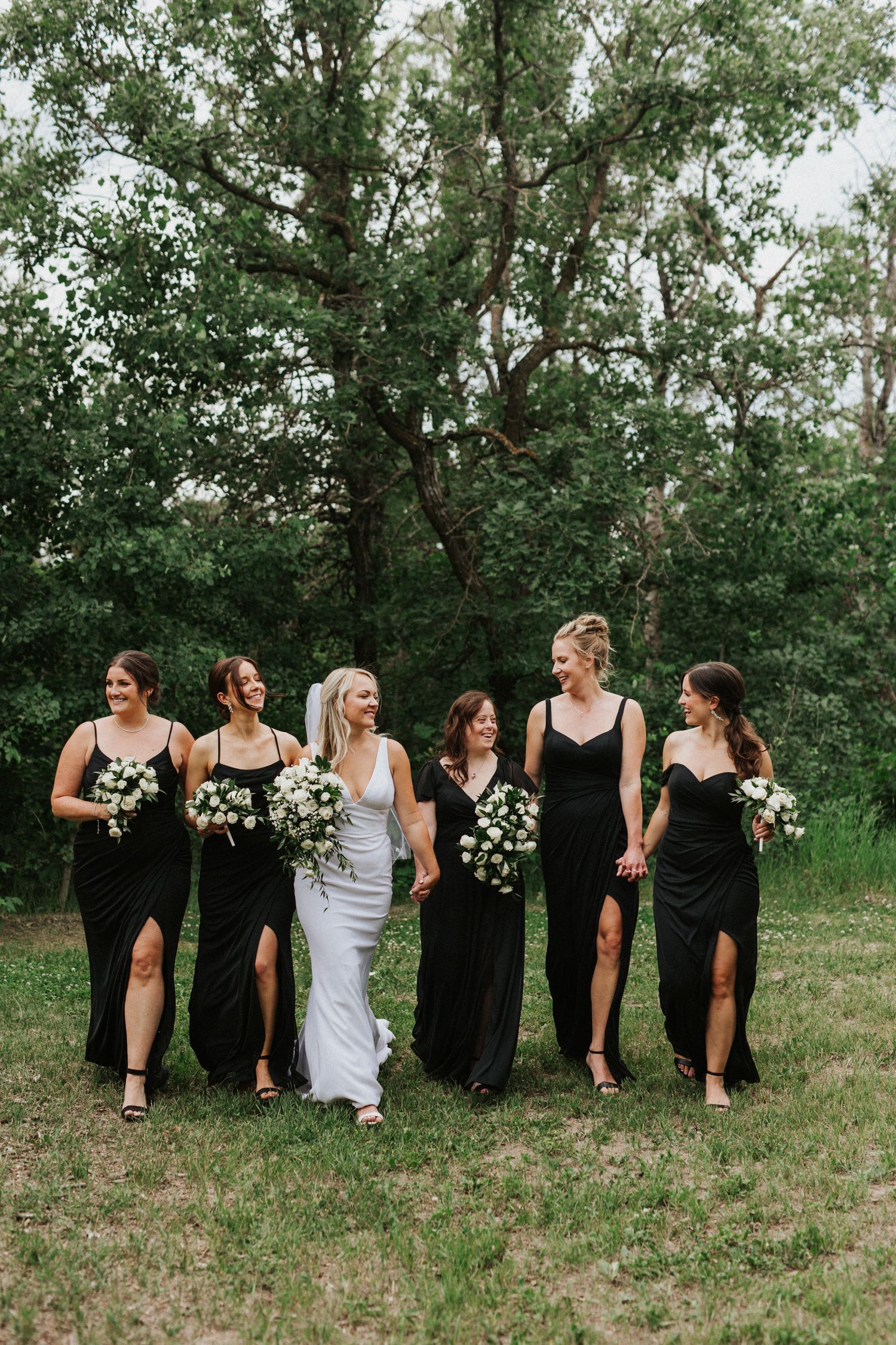 Bridesmaids in black dresses pose in a line against a natural outdoor backdrop.