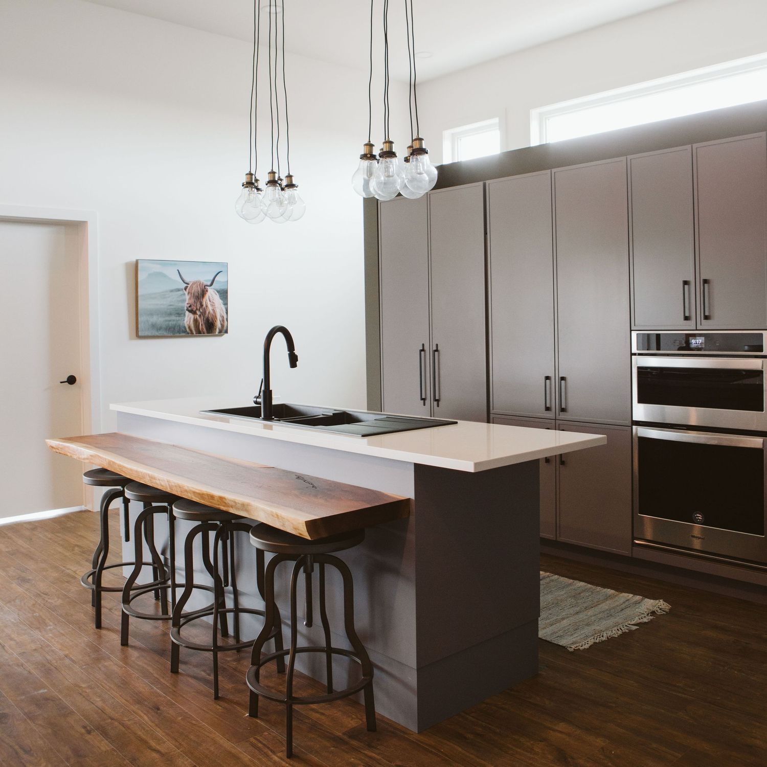 Modern kitchen interior with wooden countertop and pendant lighting showcasing minimalist design and dark cabinetry.