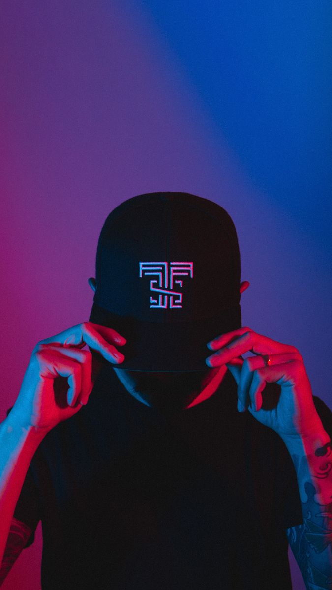 Black cap with white logo photographed against blue and purple gradient lighting.