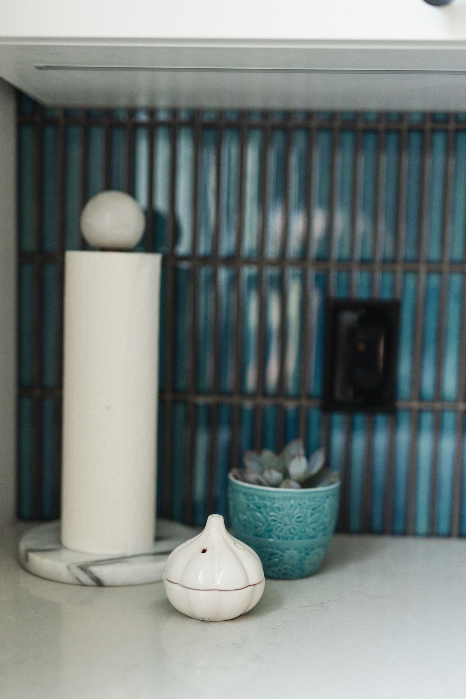 Blue tiled backsplash with white ceramic containers and decor items on shelf.