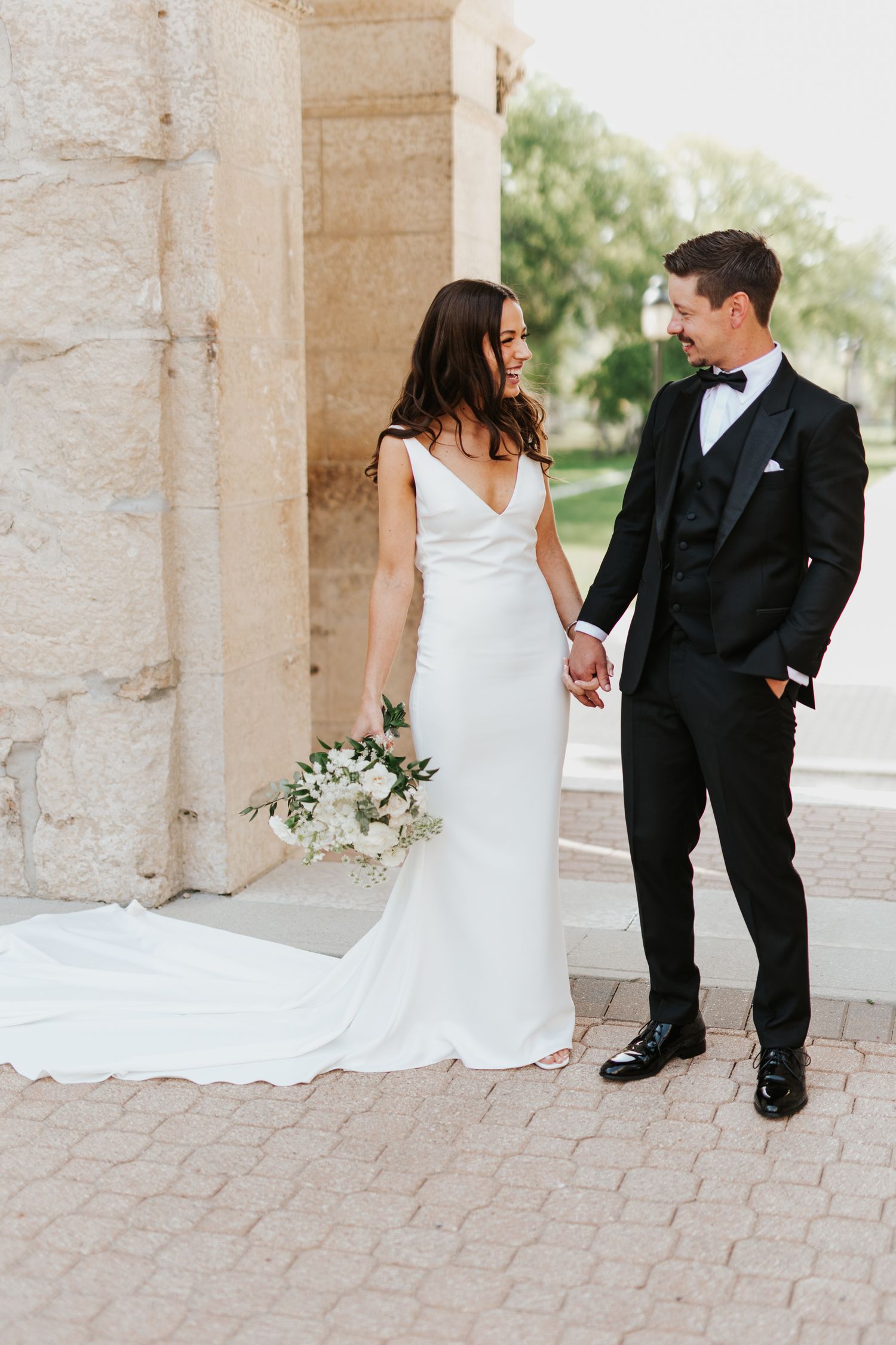 Wedding couple stands in elegant poses between stone pillars for romantic portraits.