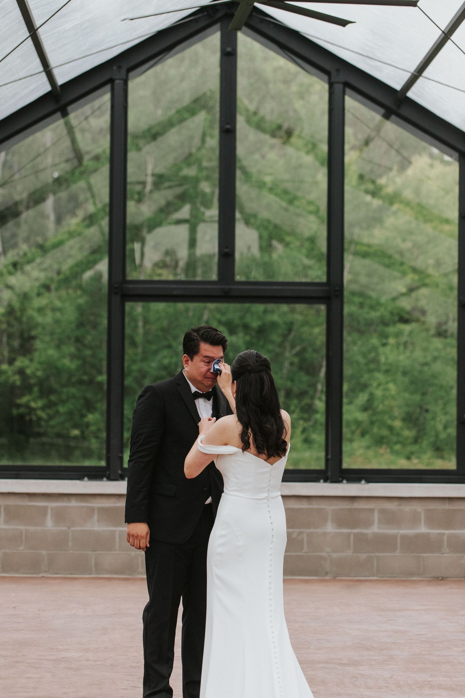 A romantic wedding moment captured in a modern greenhouse with floor-to-ceiling windows.