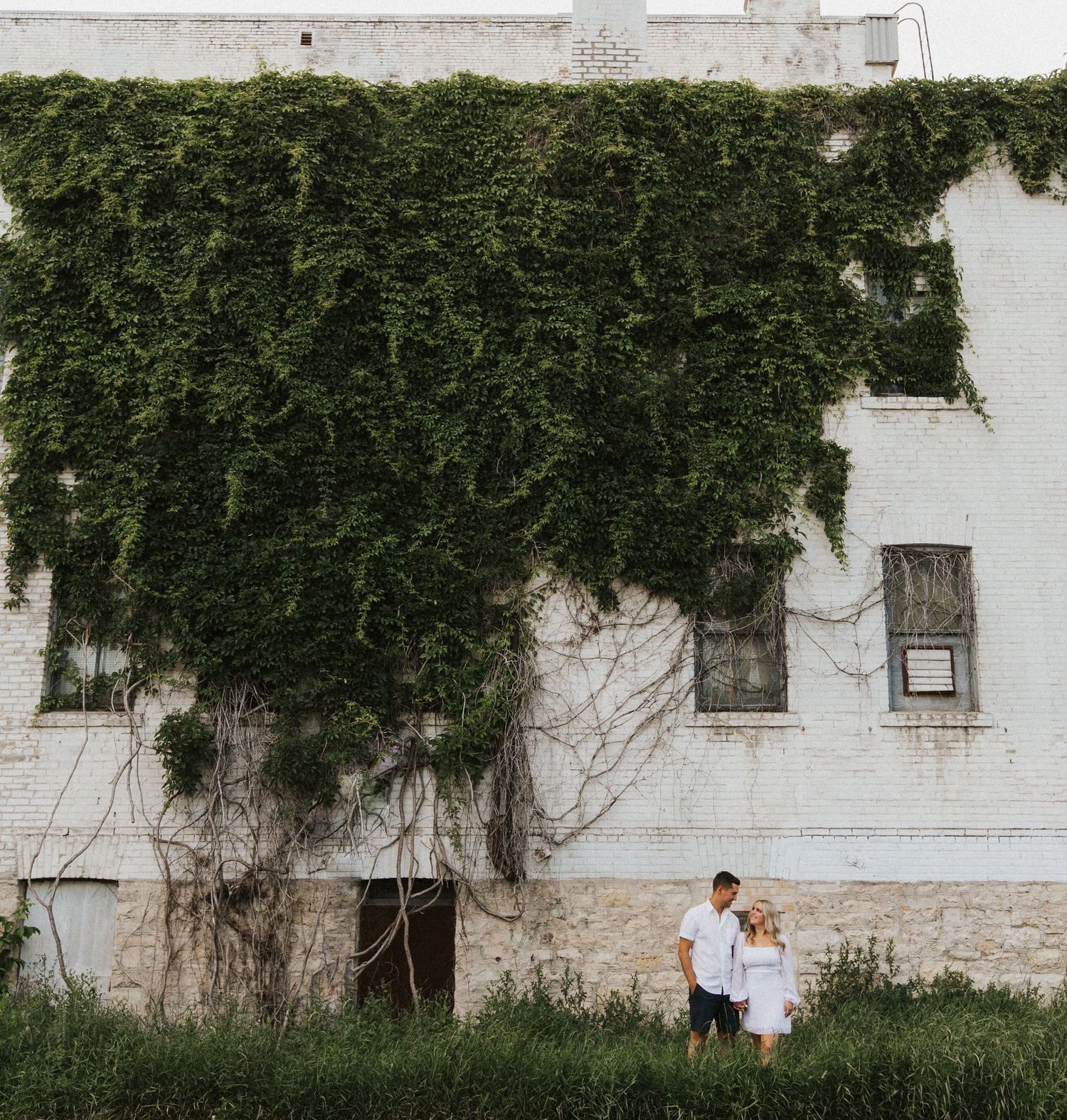 Natural progression of couple walking along ivy-covered white building wall.
