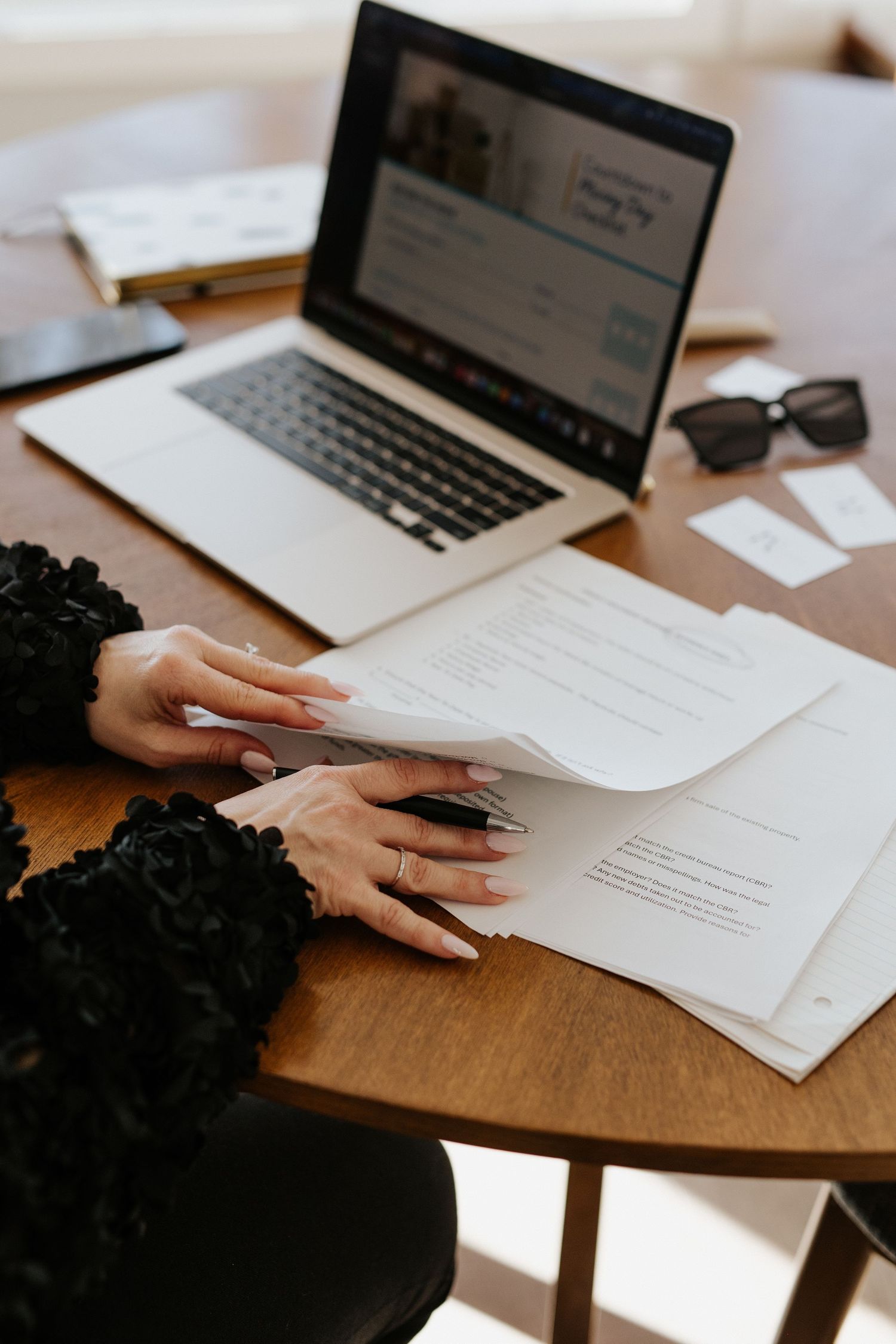 Series of hands reviewing documents and working on laptops at a wooden desk.
