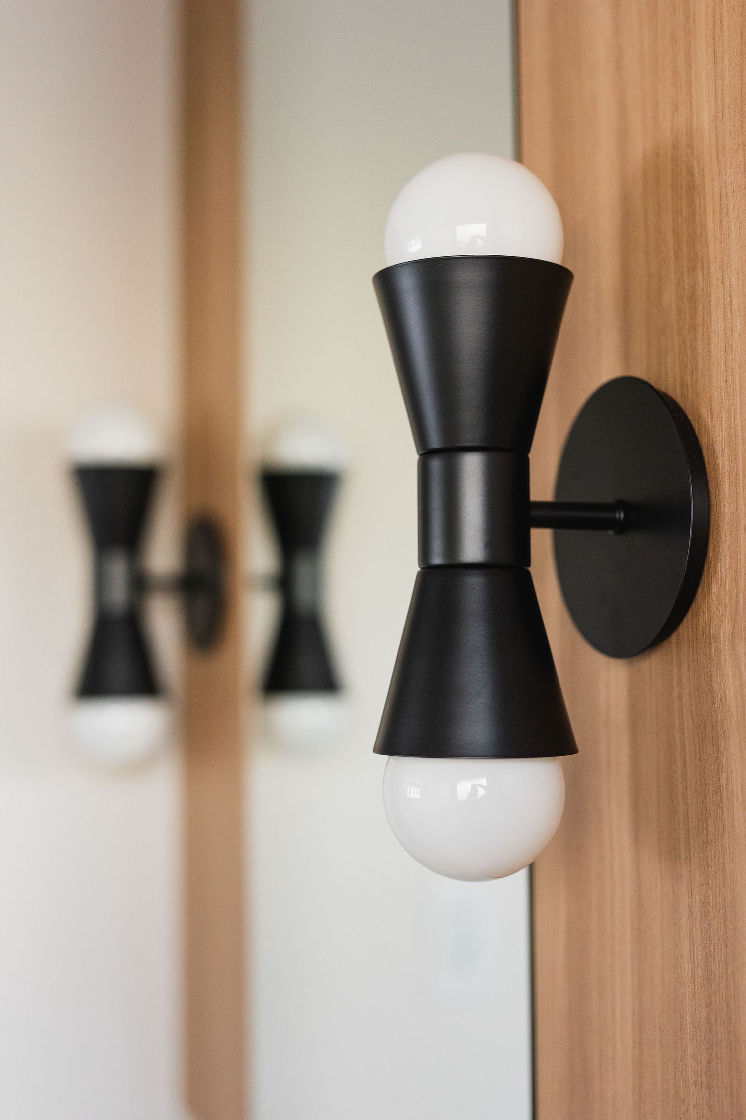 Row of modern black and white hourglass-shaped wall sconces mounted on wooden paneling.