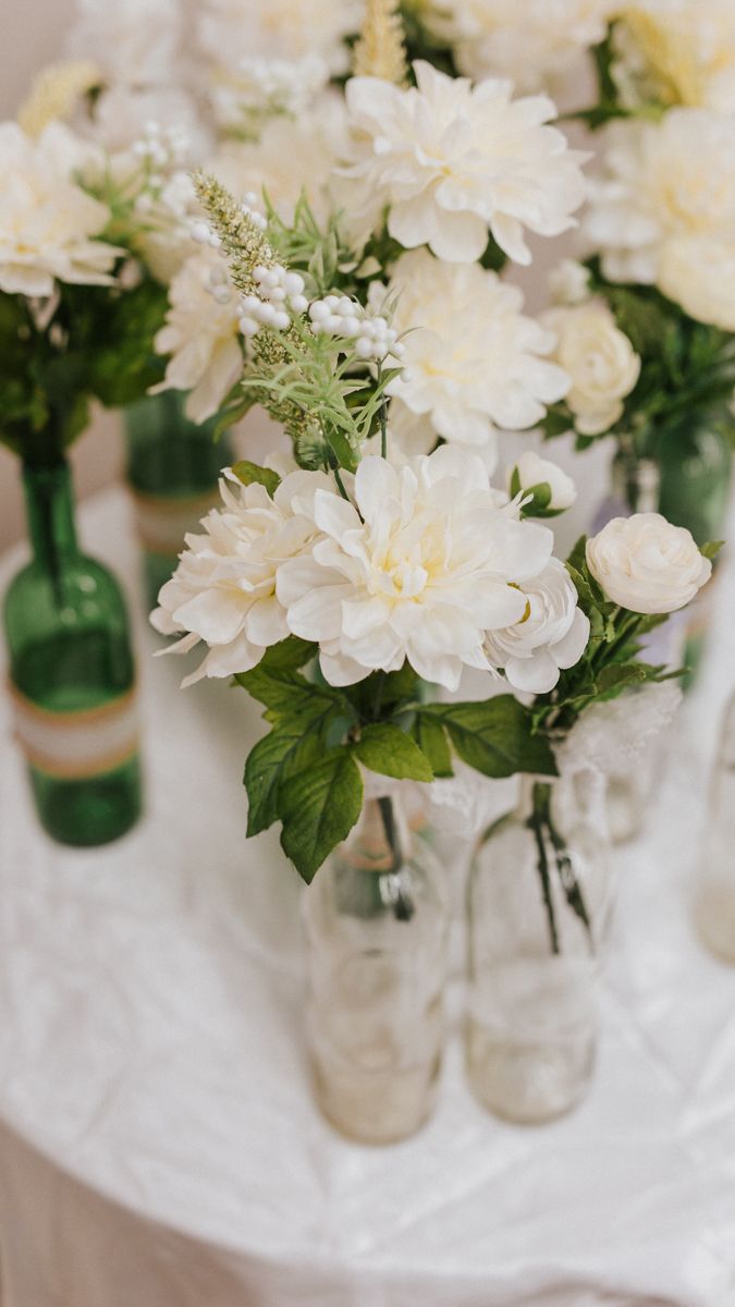 White carnations and greenery arranged in glass vases on a light colored surface.