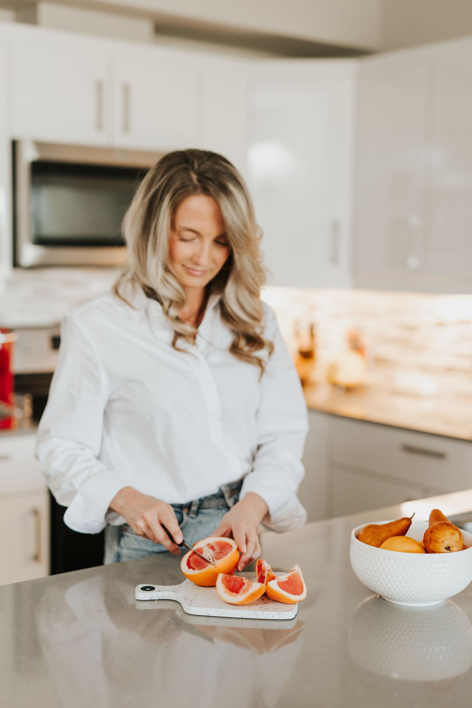 Person in white blouse slicing fresh grapefruit in modern kitchen.