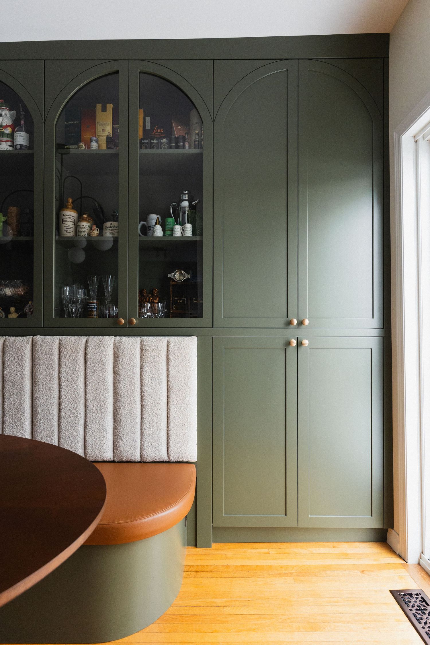 Built-in sage green cabinetry with curved bench seating and glass storage display.