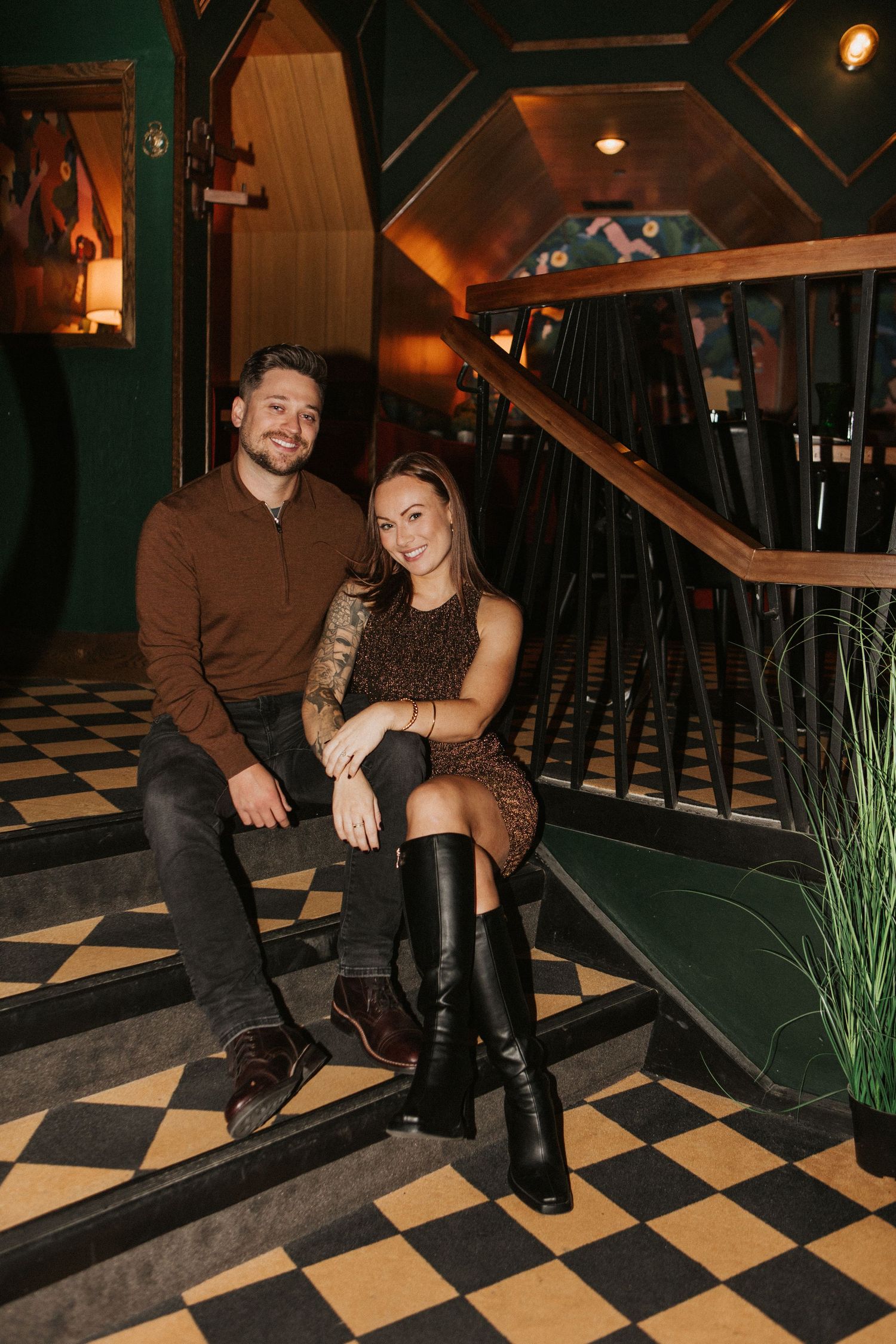 Couple seated on checkered floor in stylish evening attire at restaurant.