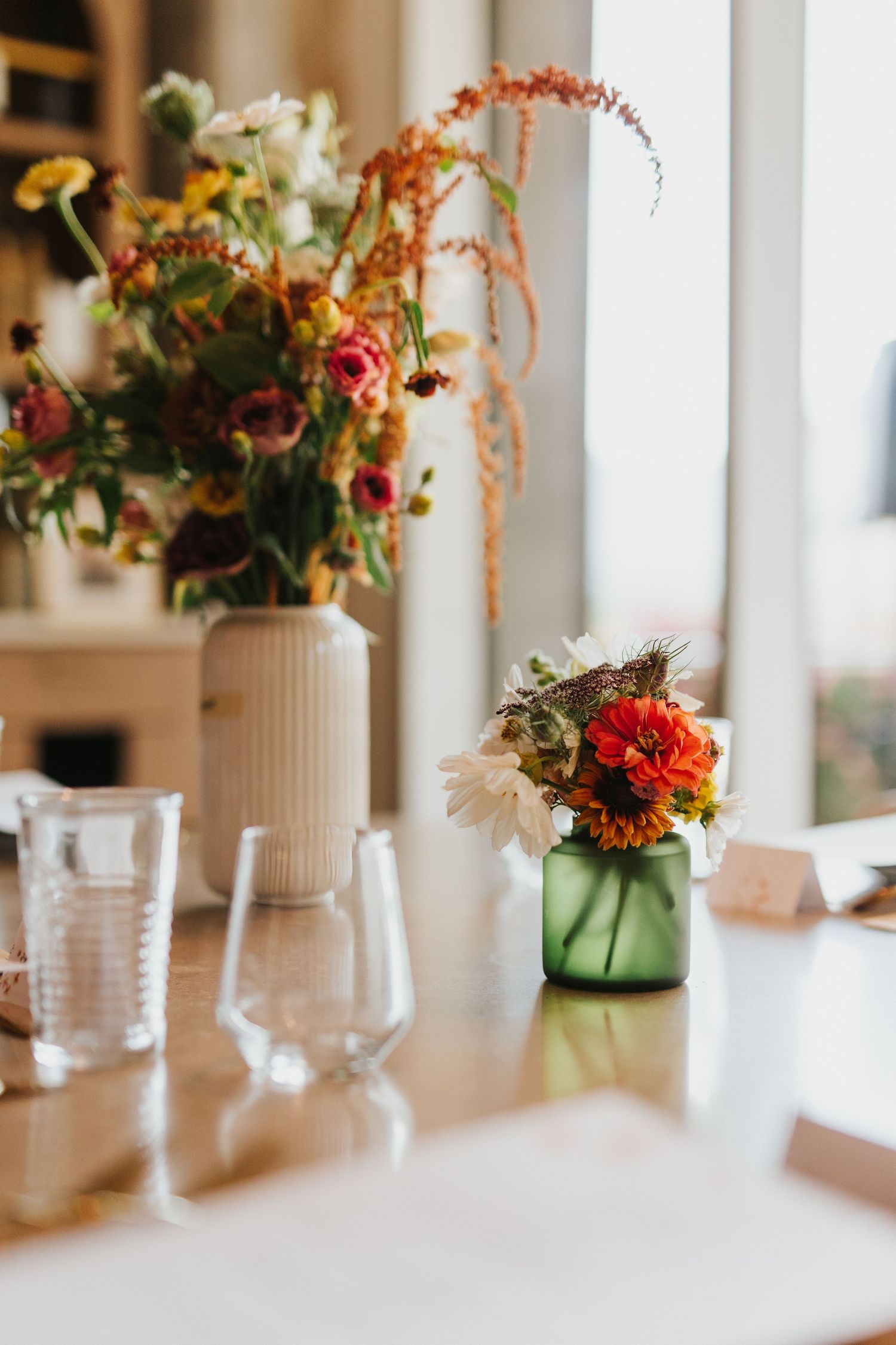 Bright floral centerpieces with colorful blooms in green vases on wedding reception tables.