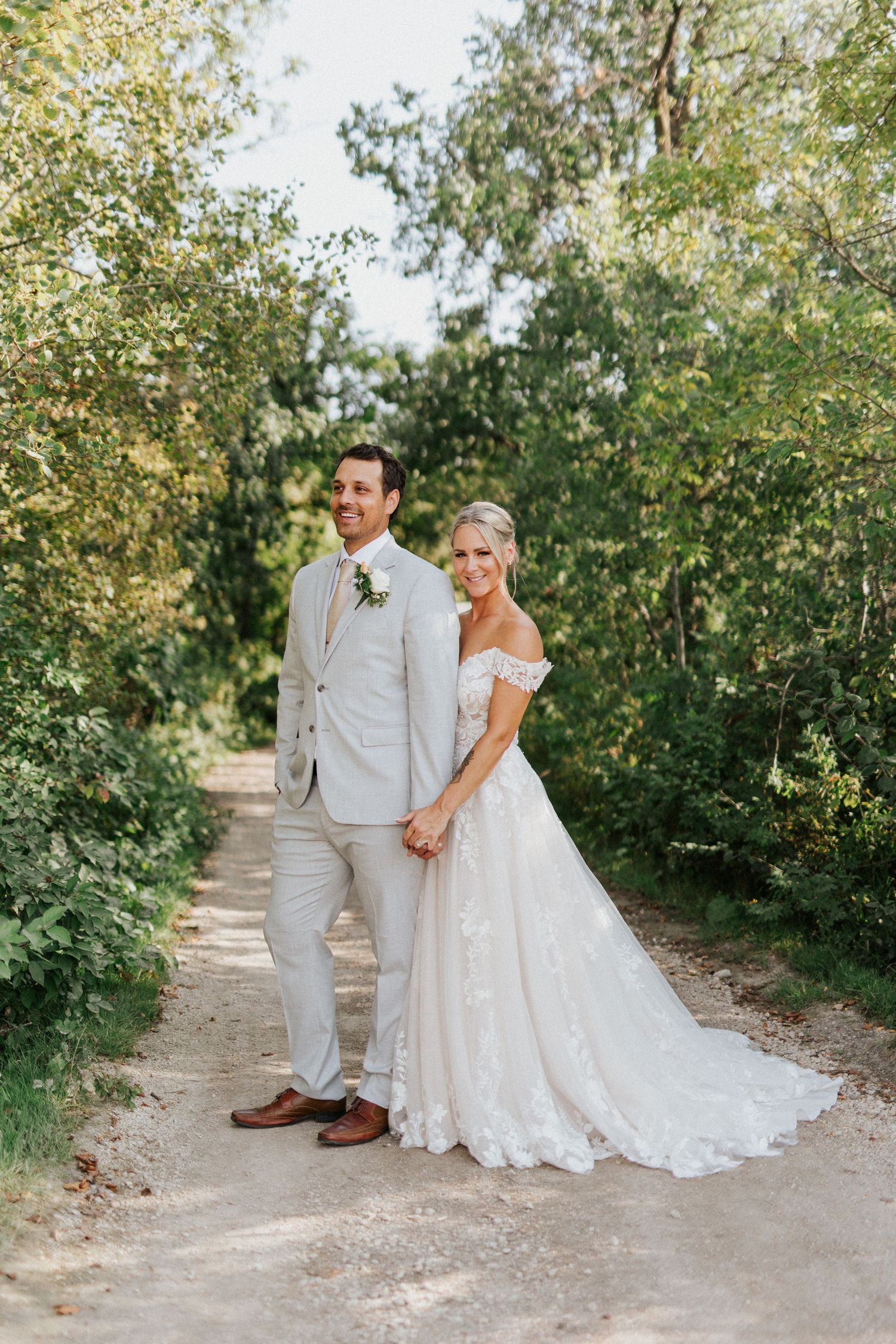 A wedding couple poses on a garden path surrounded by lush greenery.