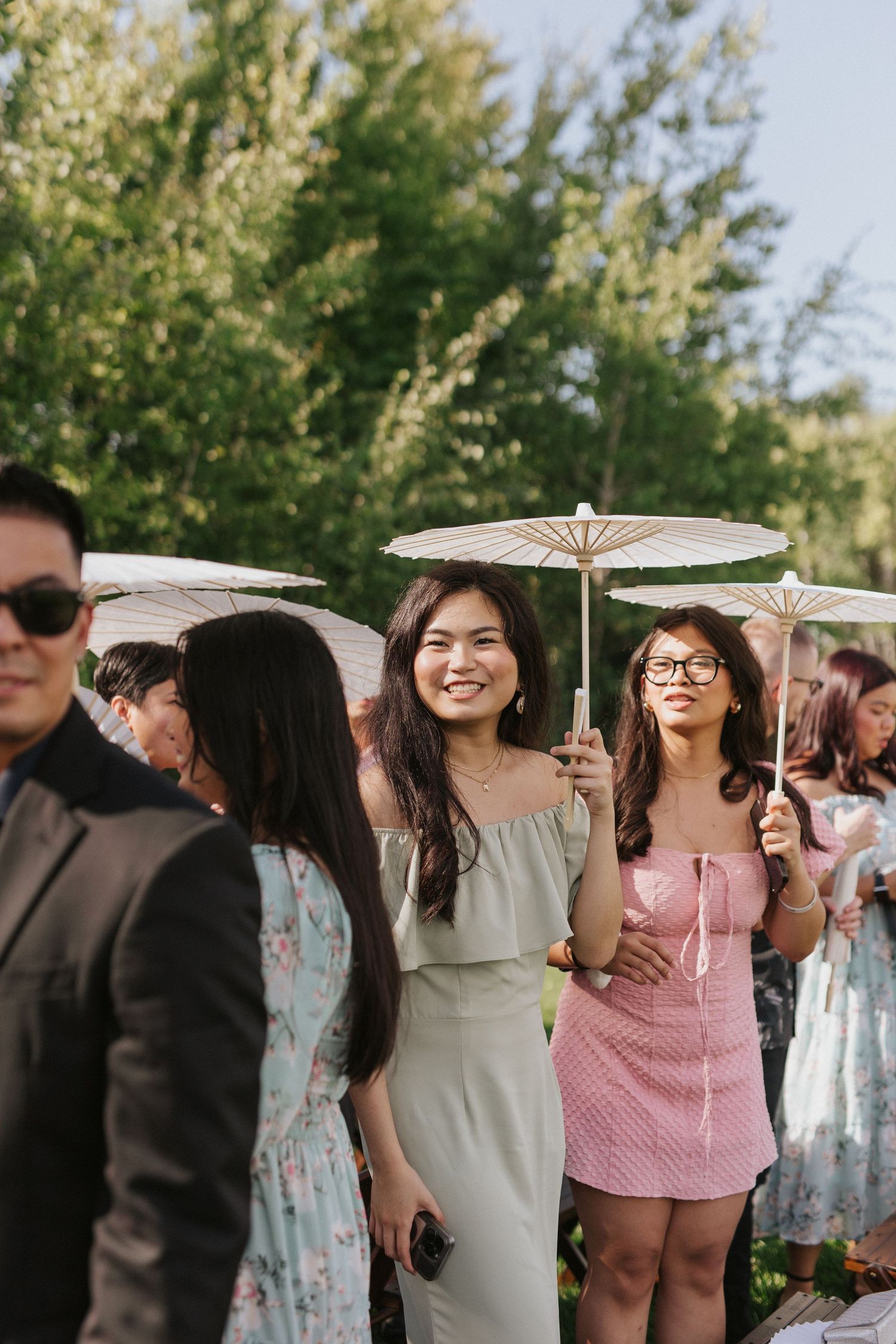 Wedding guests hold decorative paper parasols during an outdoor celebration.