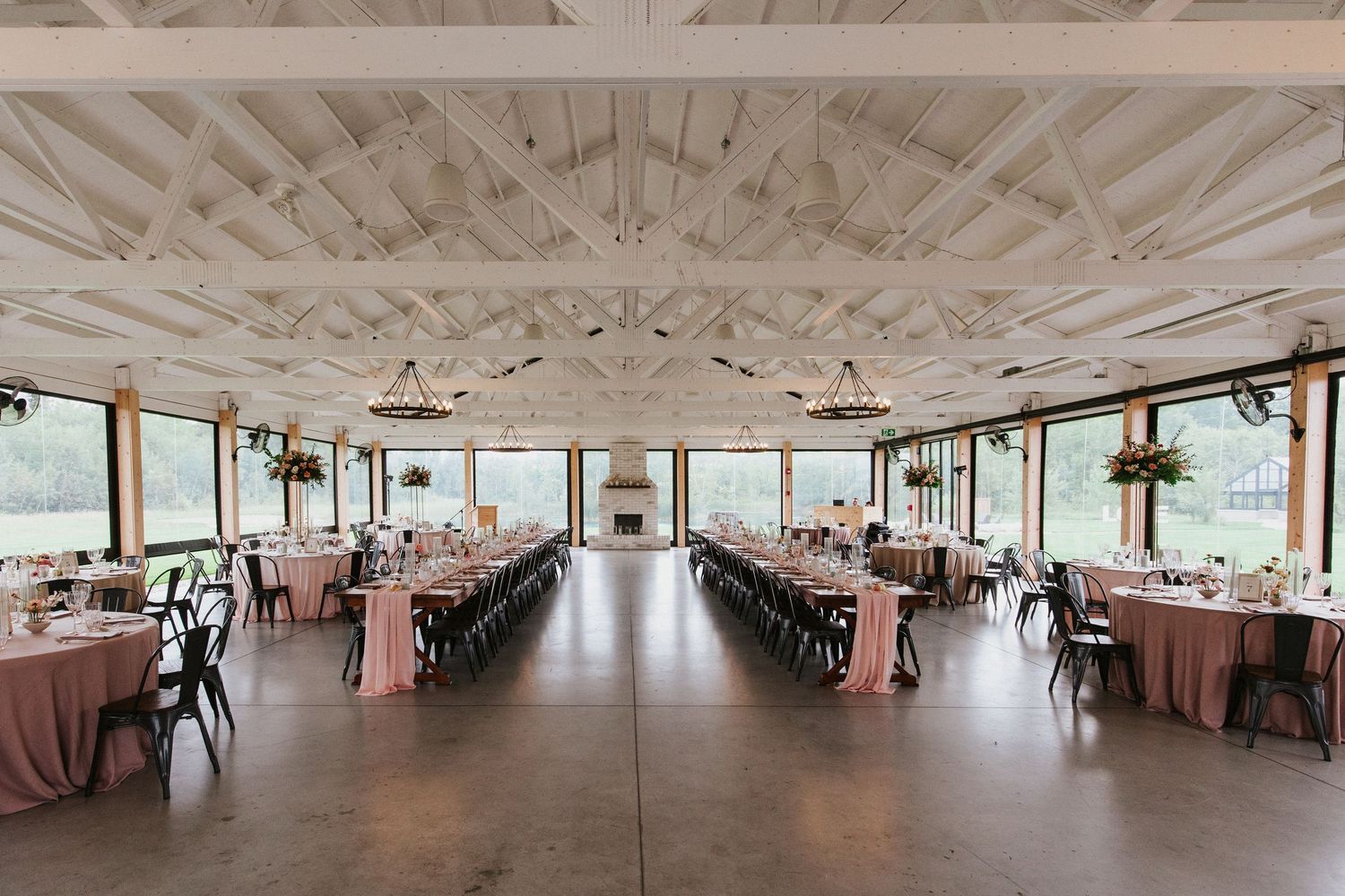 Panoramic view of an elegant wedding reception venue with pink and white decor and wooden ceiling beams.