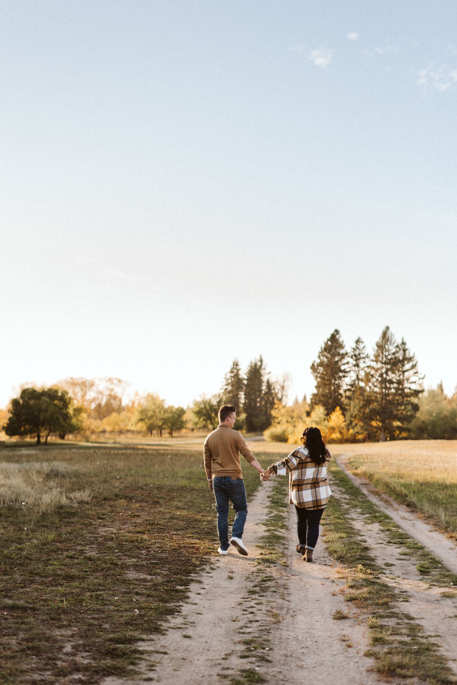 Couple walking hand in hand down a rural dirt path during golden hour.