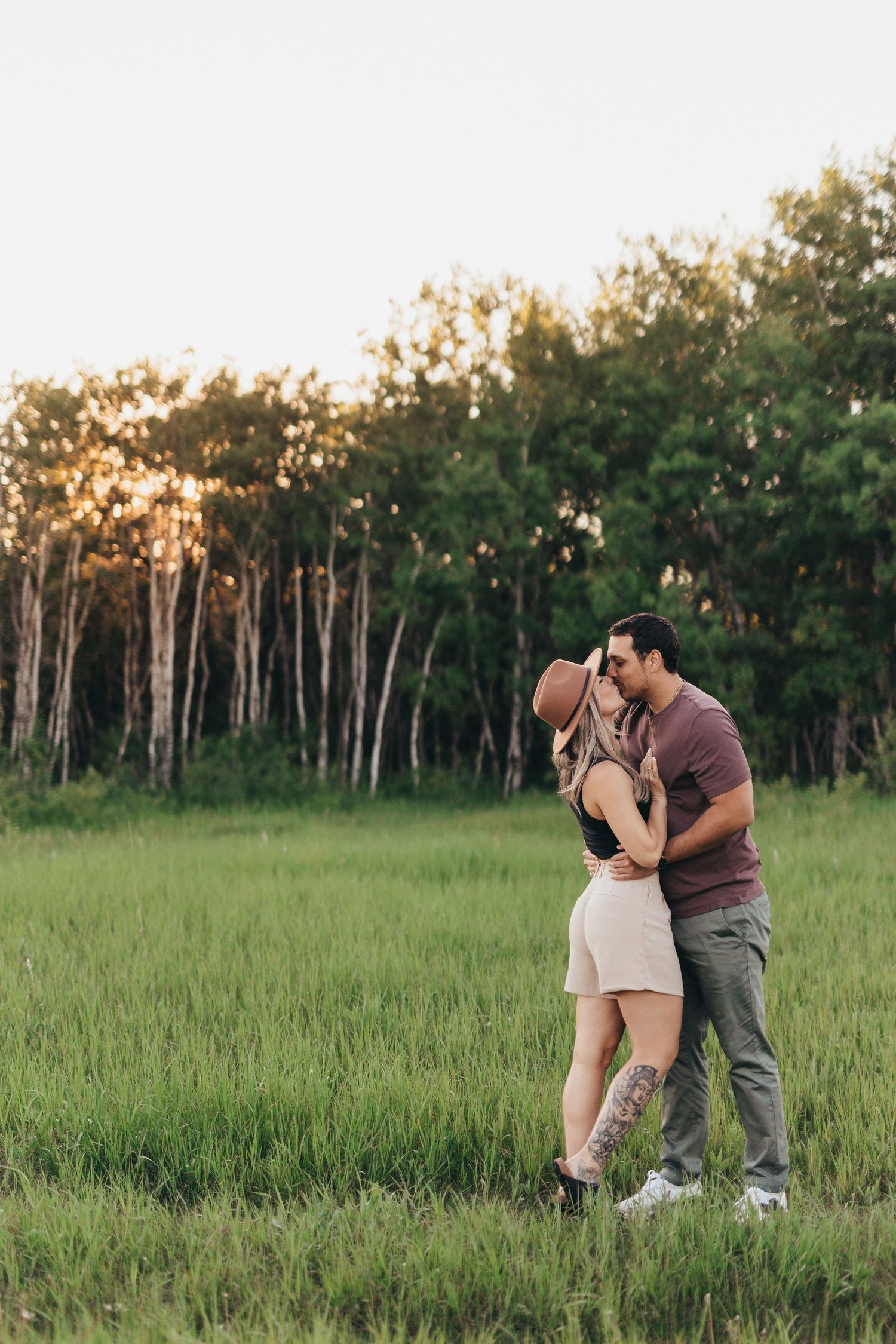 Couple embraces in golden sunlight among tall grasses and birch trees.