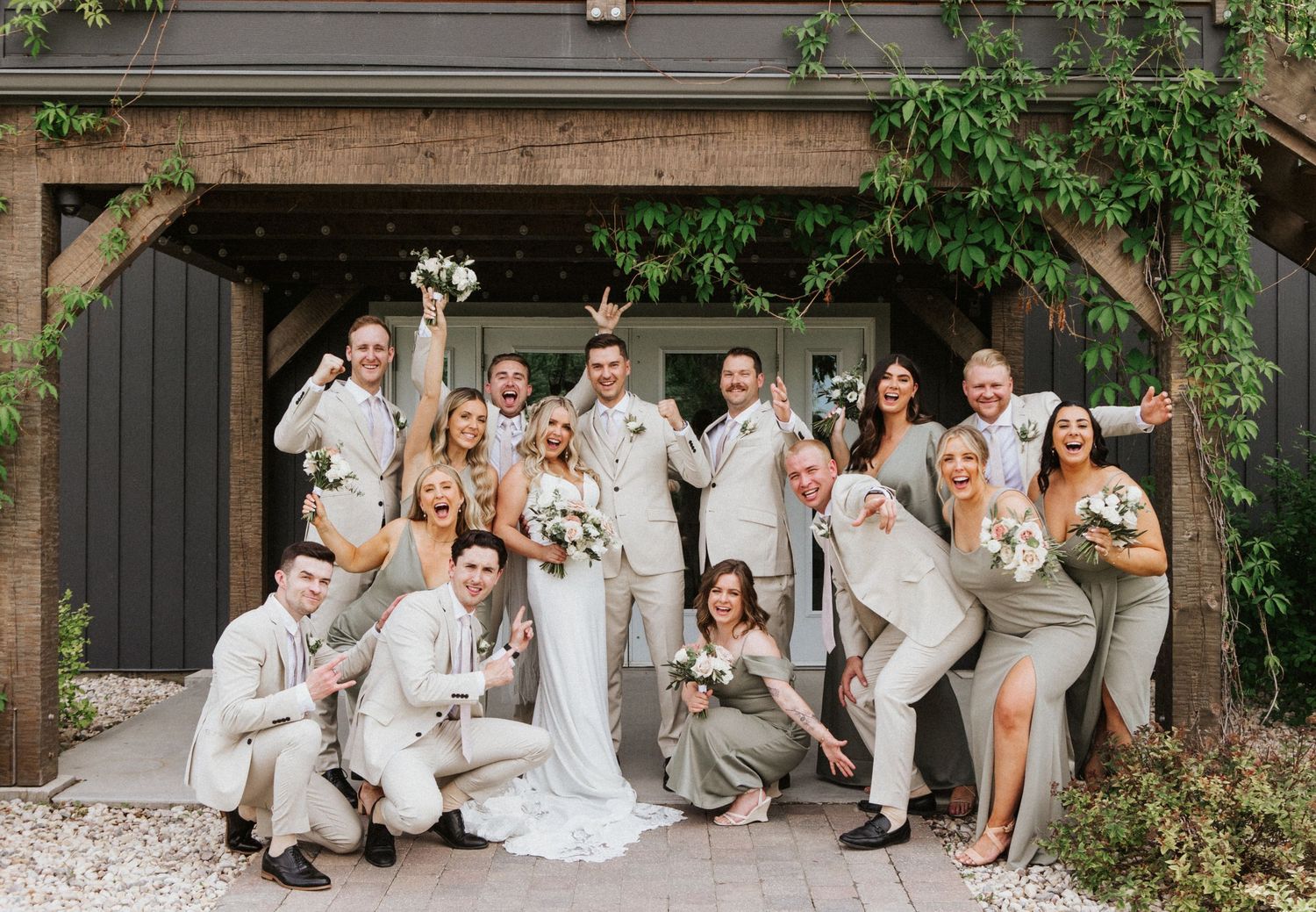 Wedding party in white and neutral attire poses playfully together on stone patio.