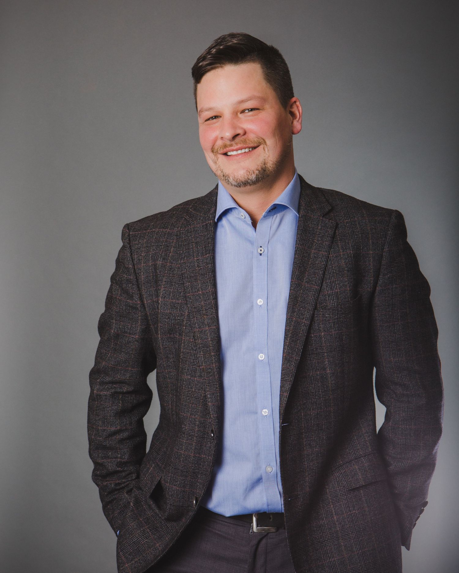 Professional business portrait in charcoal suit and light blue shirt against grey background.