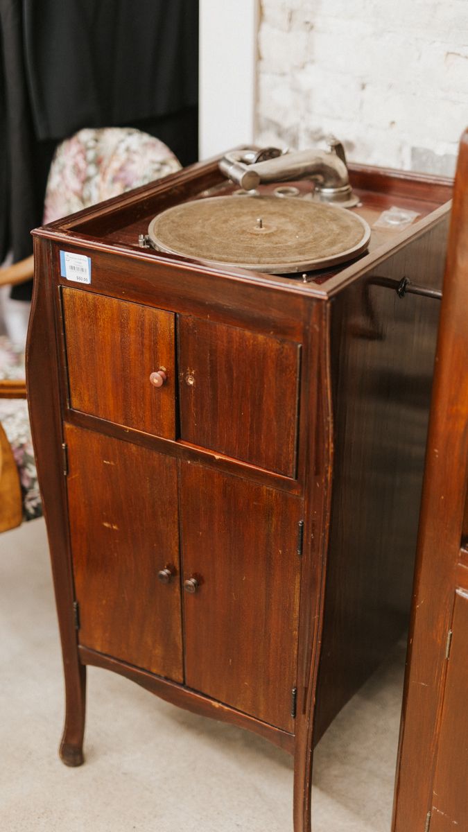 Vintage wooden bedside table with cabinet doors and legs displayed in antique store.