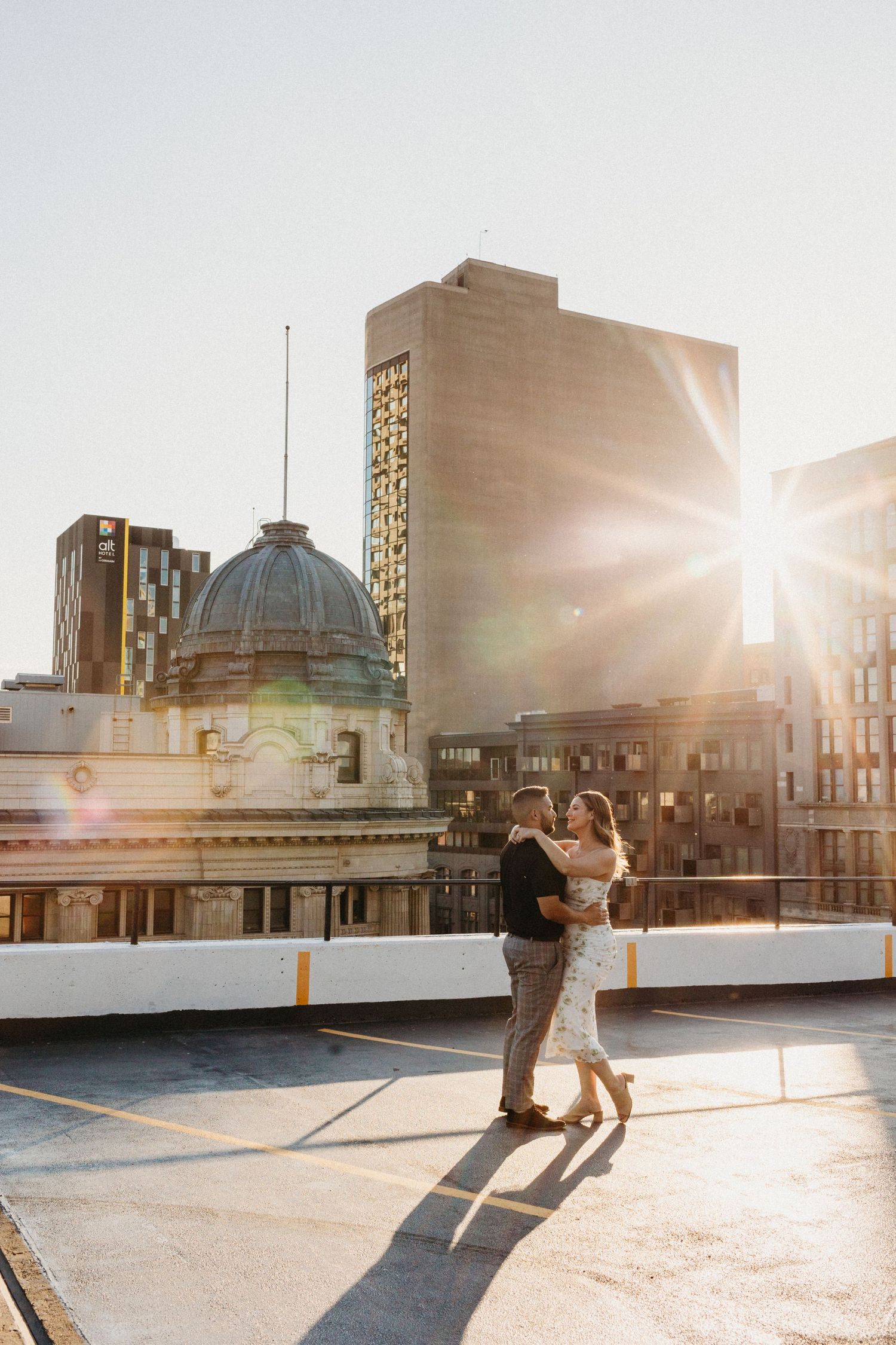 Couple dances on rooftop with urban skyline and sunset backdrop.