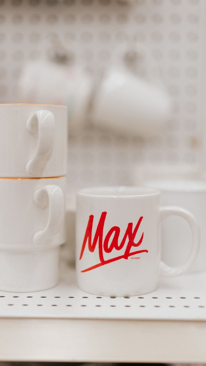 White ceramic coffee mugs with red text displayed in a minimalist setting.