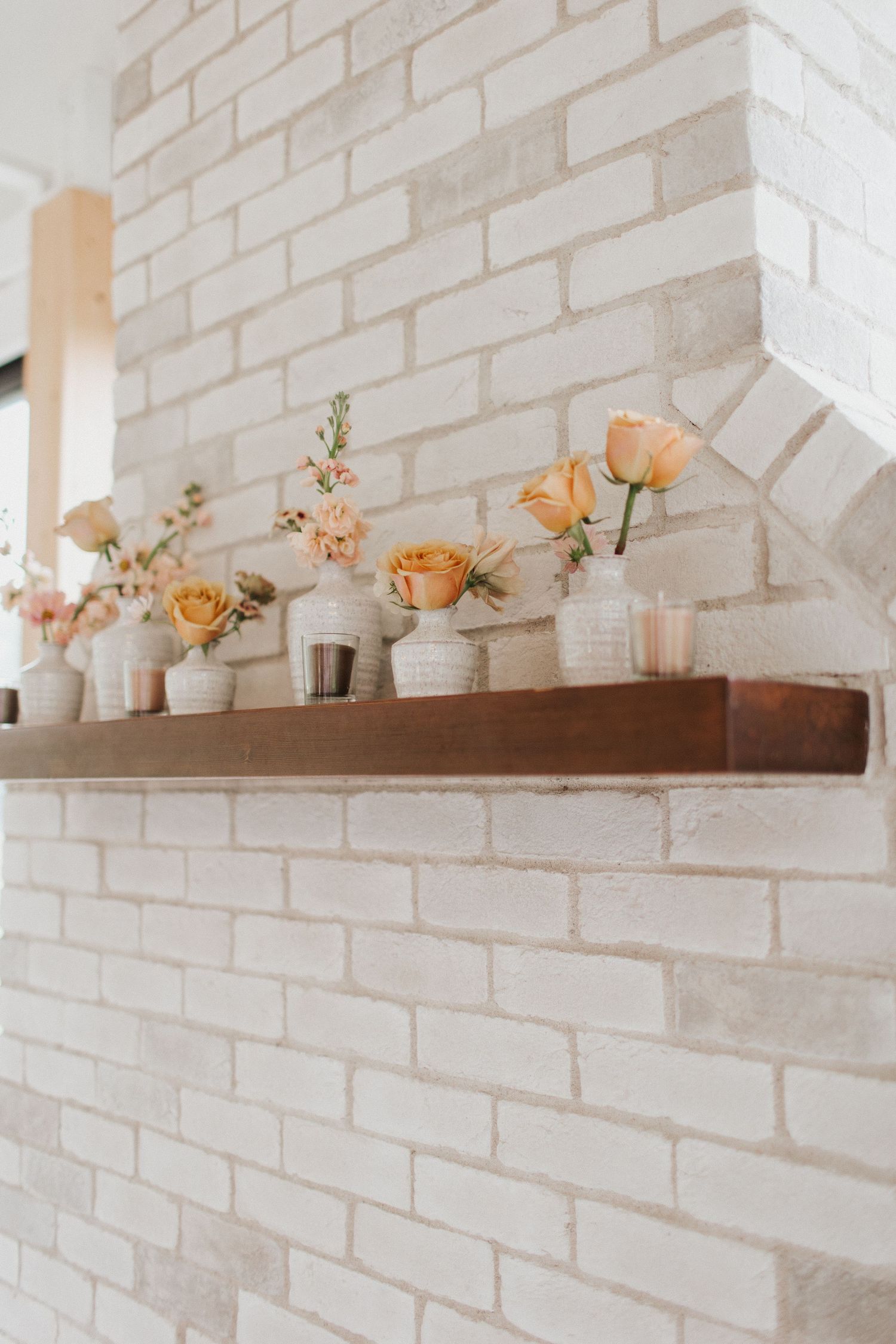 Wooden floating shelf with peach roses and white ceramic vases against white painted brick wall.