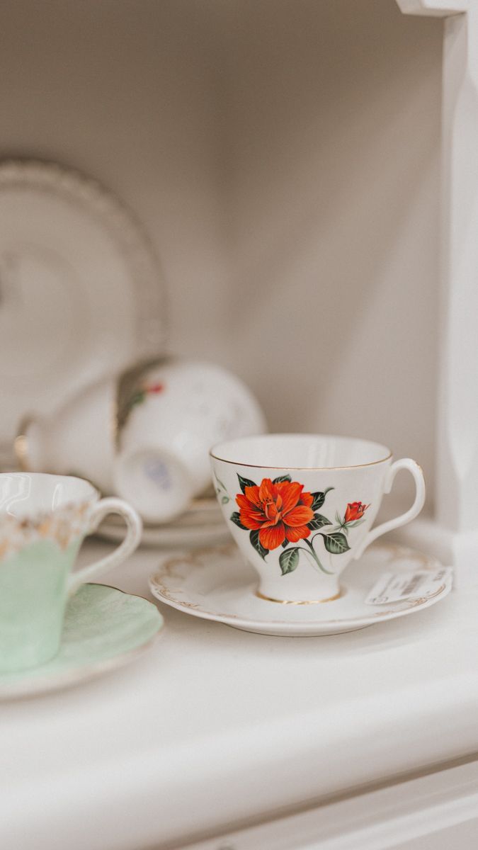 White teacup with red poppy flower design and gold trim sitting on a shelf.