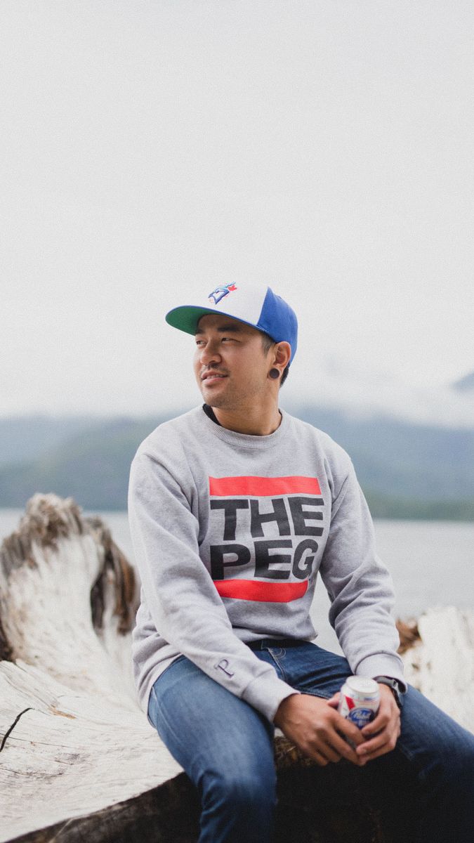Person wearing a gray sweatshirt with 'THE PEG' text sitting outdoors near water.