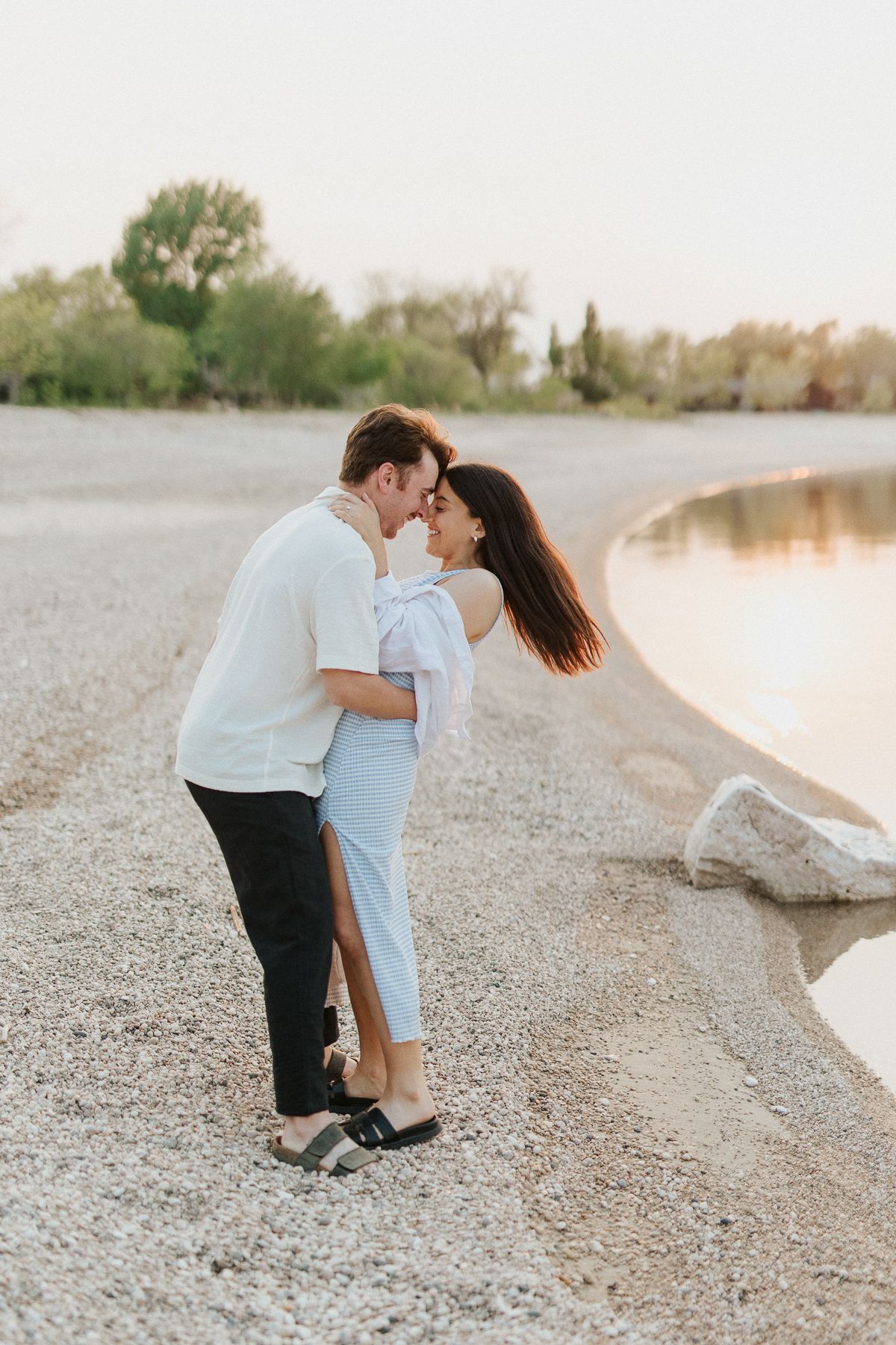 Gimli Engagement photography. Couple in coordinated outfits sharing romantic moment on pebbly beach.