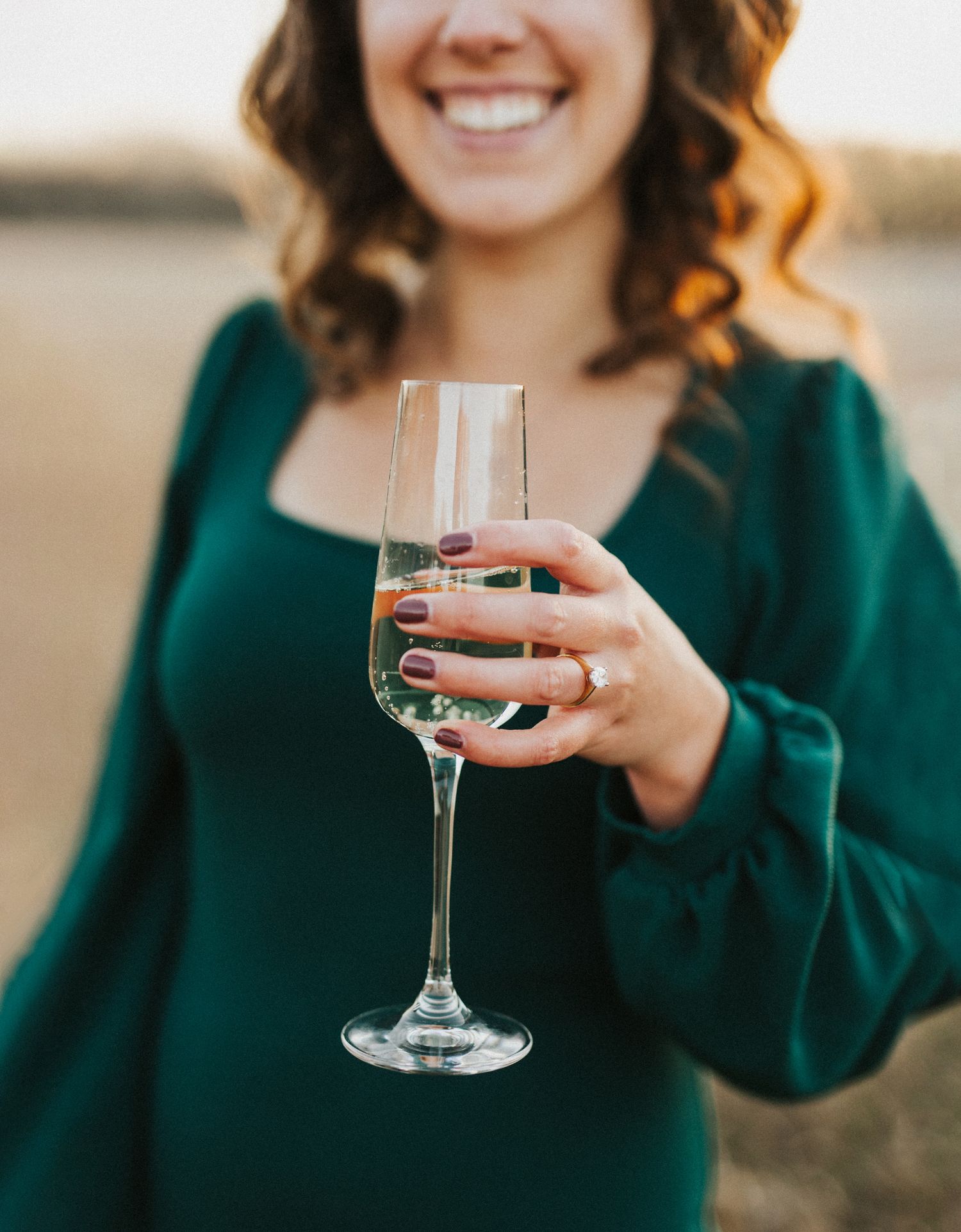 Person in emerald green sweater holding a glass of white wine at golden hour.