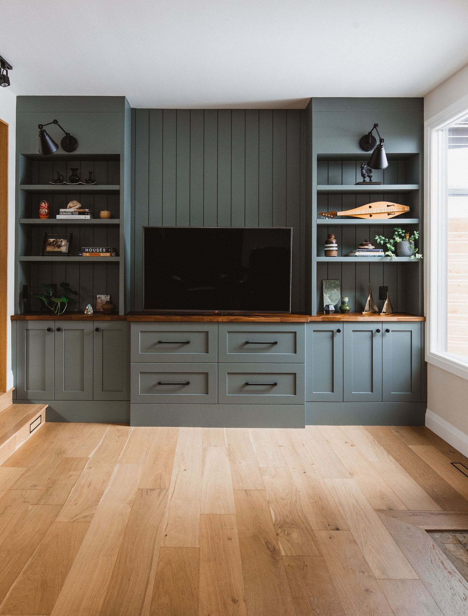 Built-in dark teal storage unit spans wall length with open shelving and cabinets over light wood flooring.
