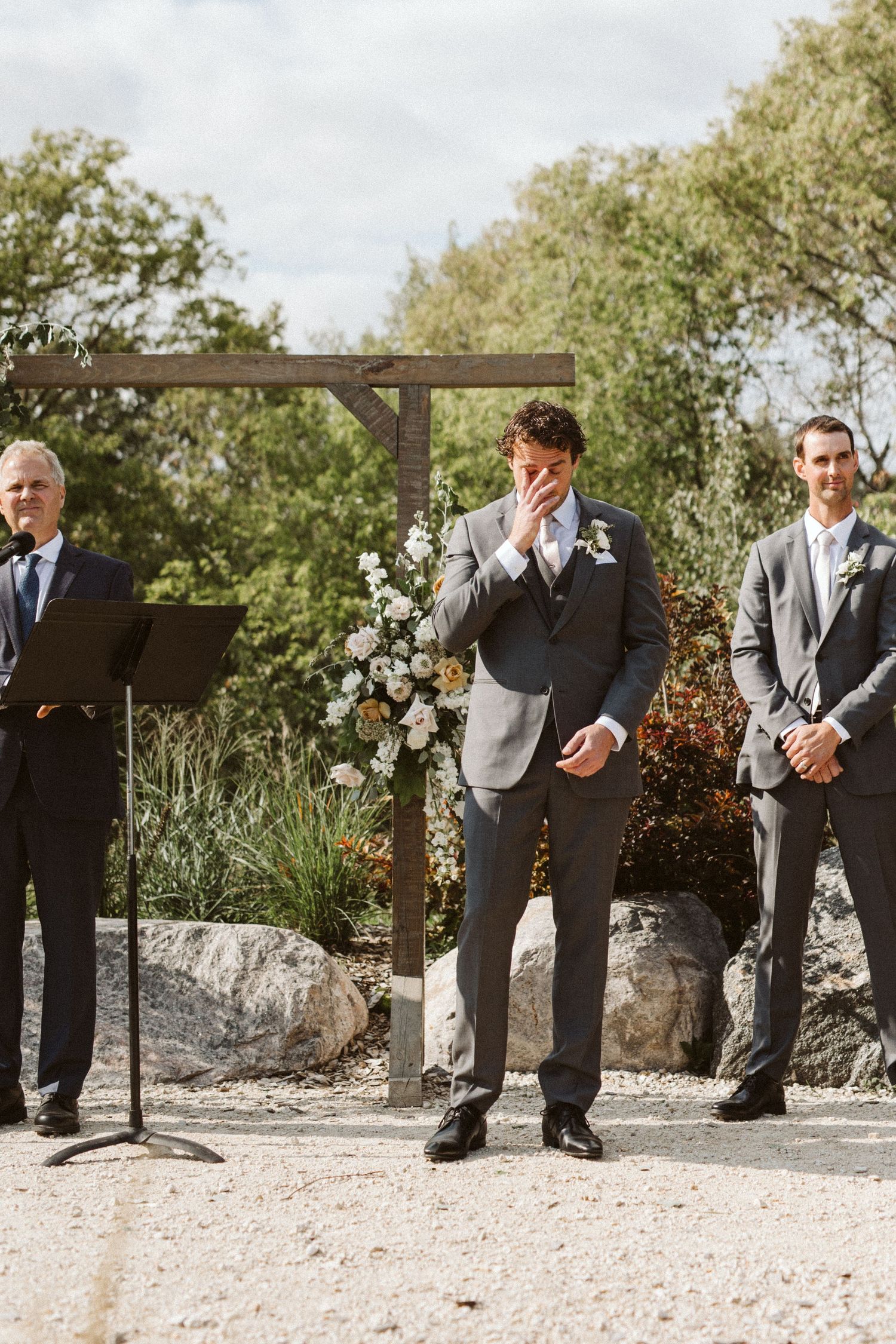 Wedding ceremony taking place under a wooden pergola with floral decorations.