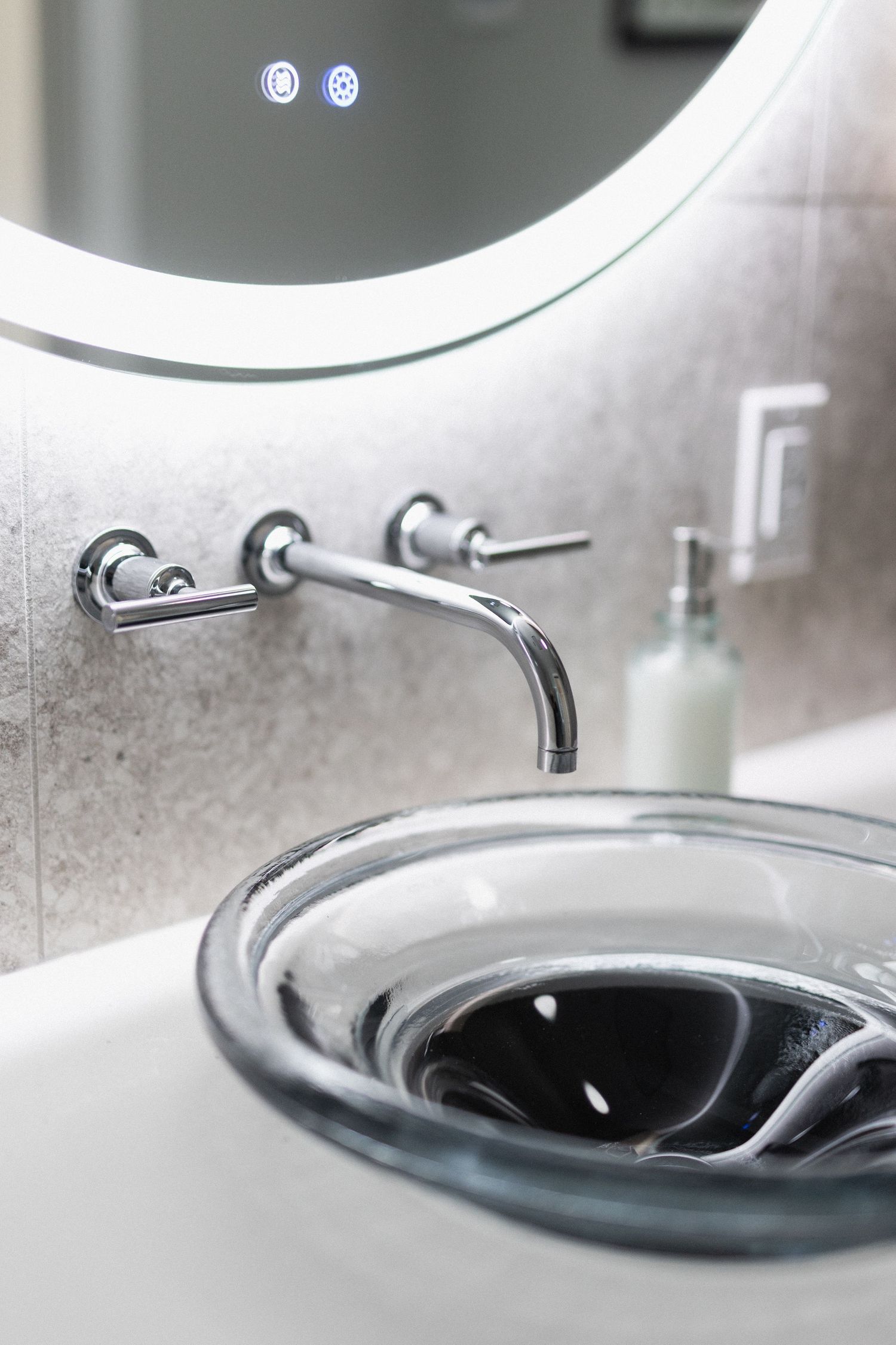 Modern bathroom sink with wall-mounted faucet and illuminated round mirror.
