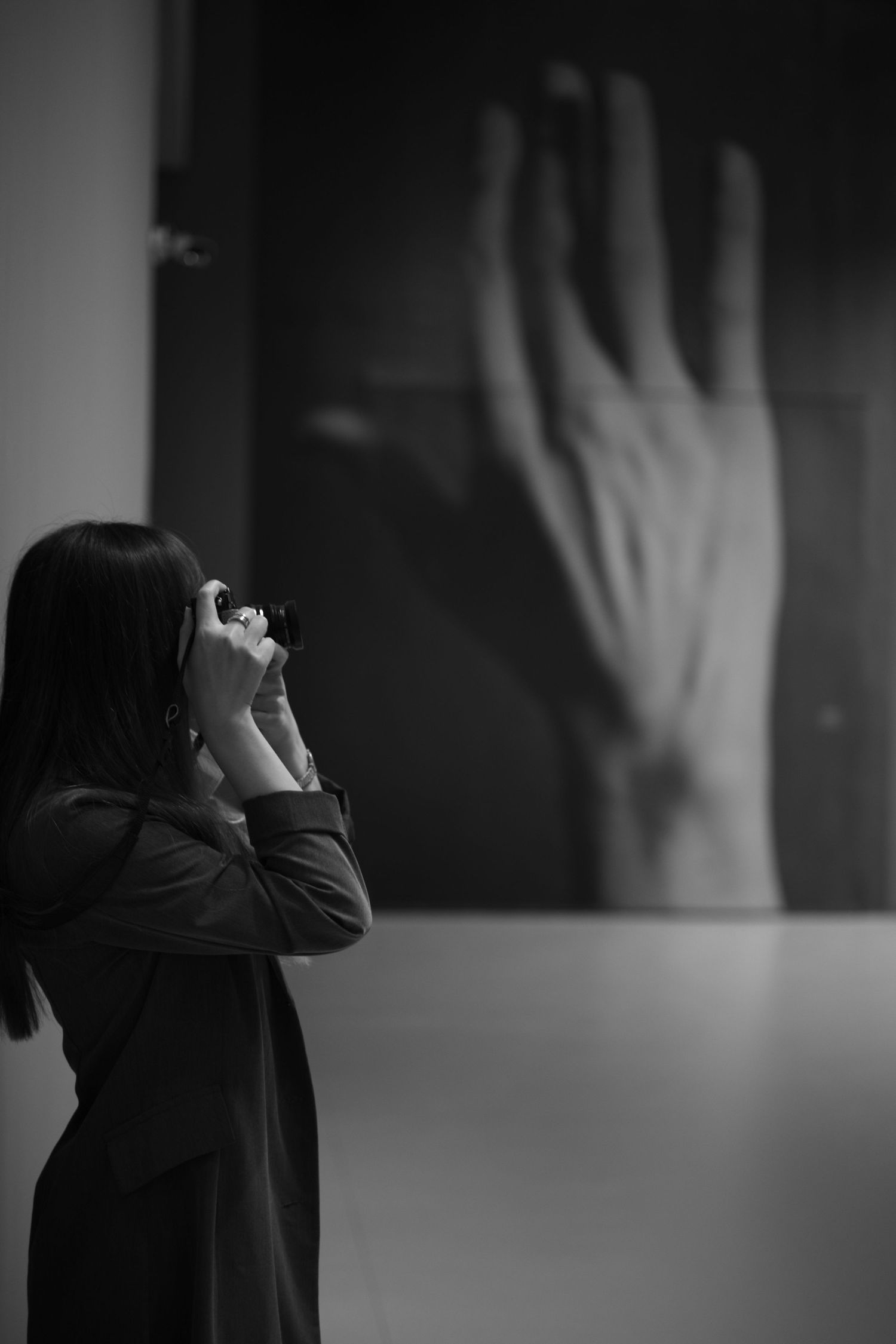 A person in glasses looks up at a large hand sculpture on display in a minimalist art gallery setting.