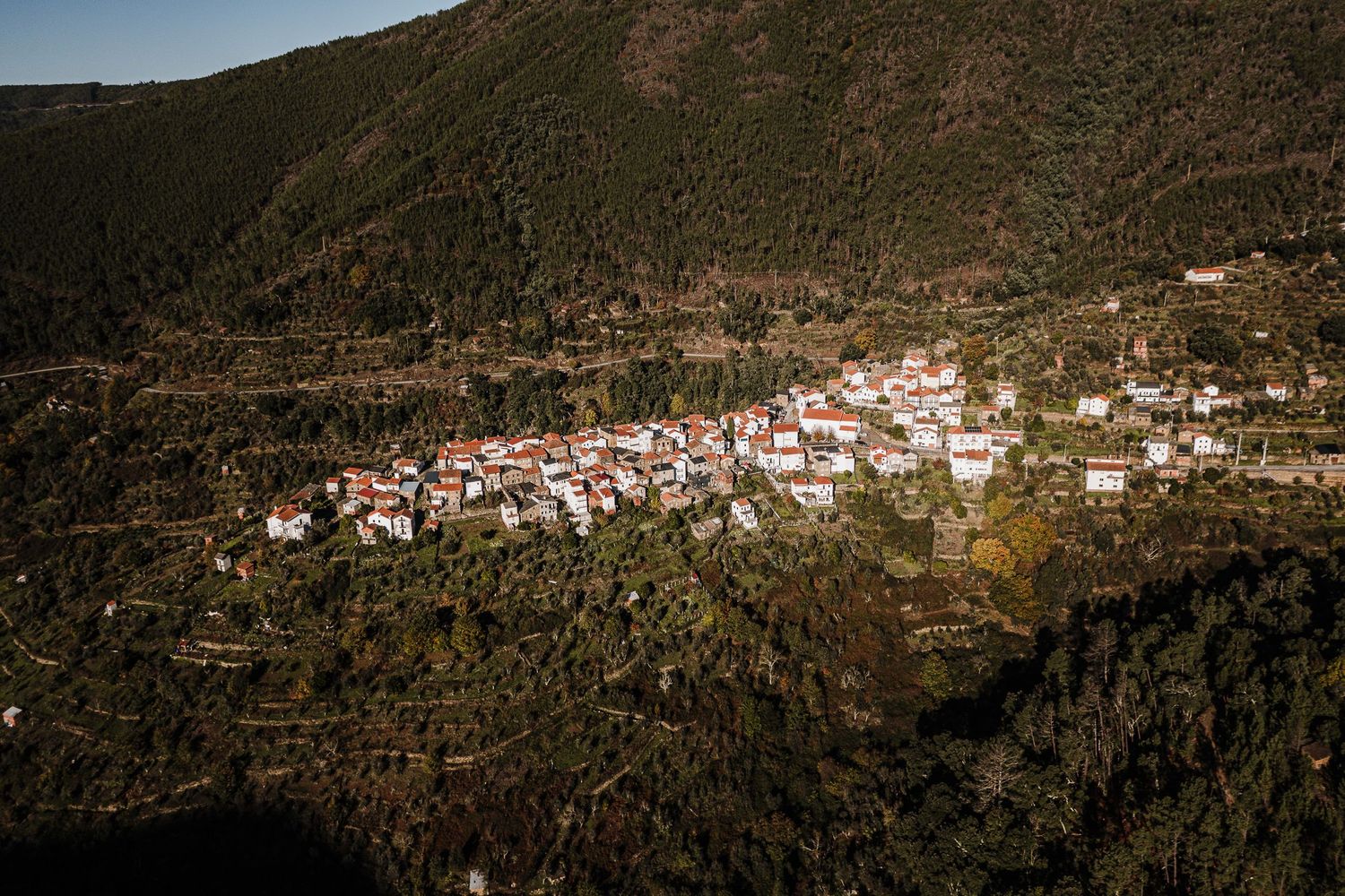 Panoramic aerial view of a small Mediterranean village nestled in the mountains with white buildings and red roofs.