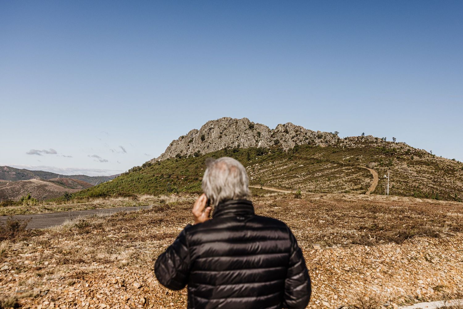 A person wearing a black puffy jacket stands on a rocky mountain peak overlooking a vast desert landscape.