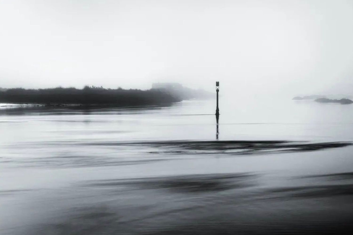 Minimalist black and white seascape with lone marker post in misty water.