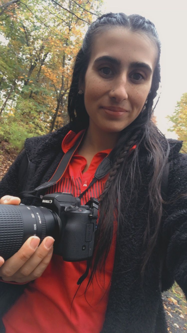 Photographer holding a DSLR camera with telephoto lens in autumn forest setting.