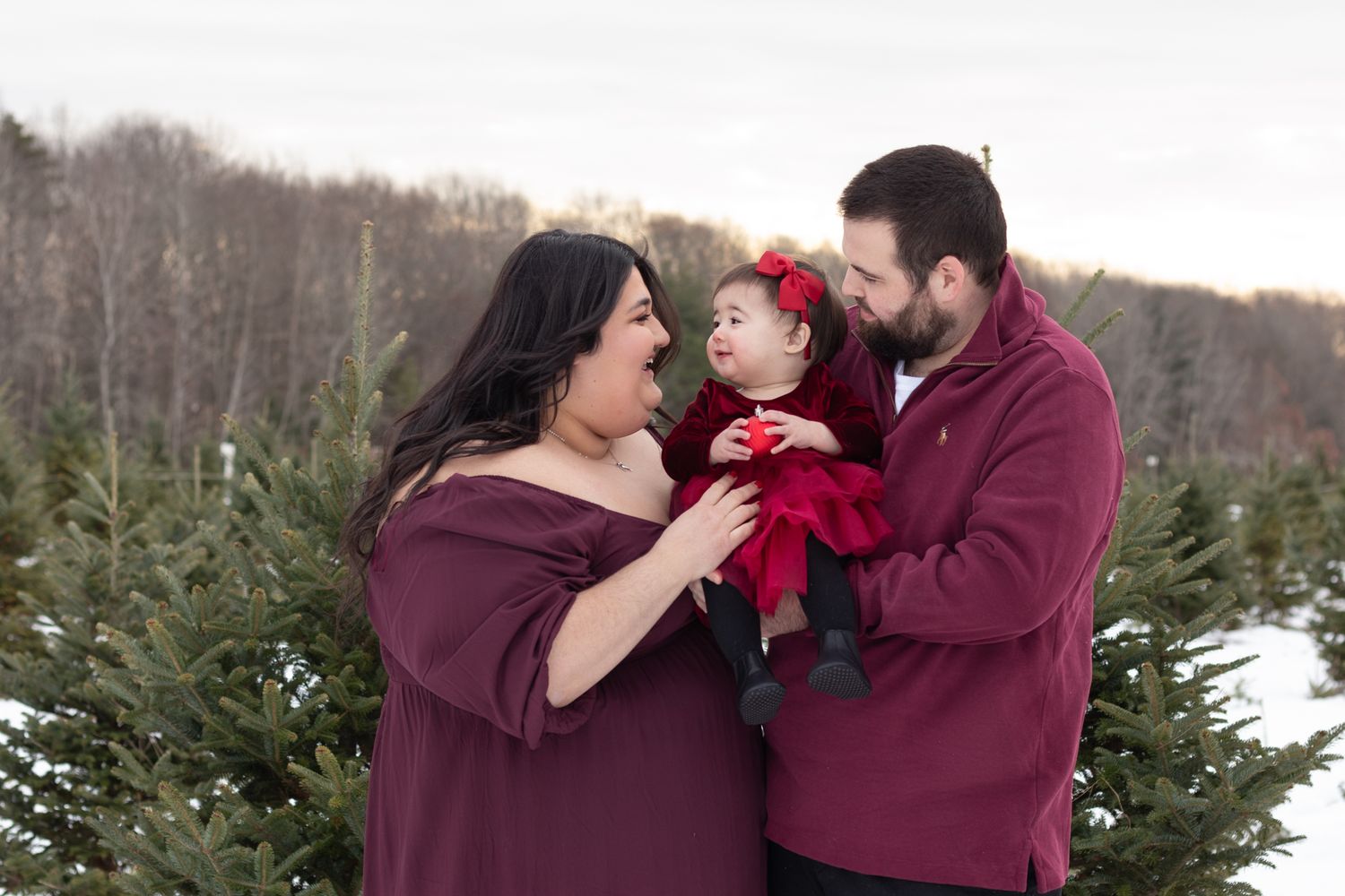 Winter family portrait among evergreen trees in matching burgundy outfits at John lLyden Tree Farm.