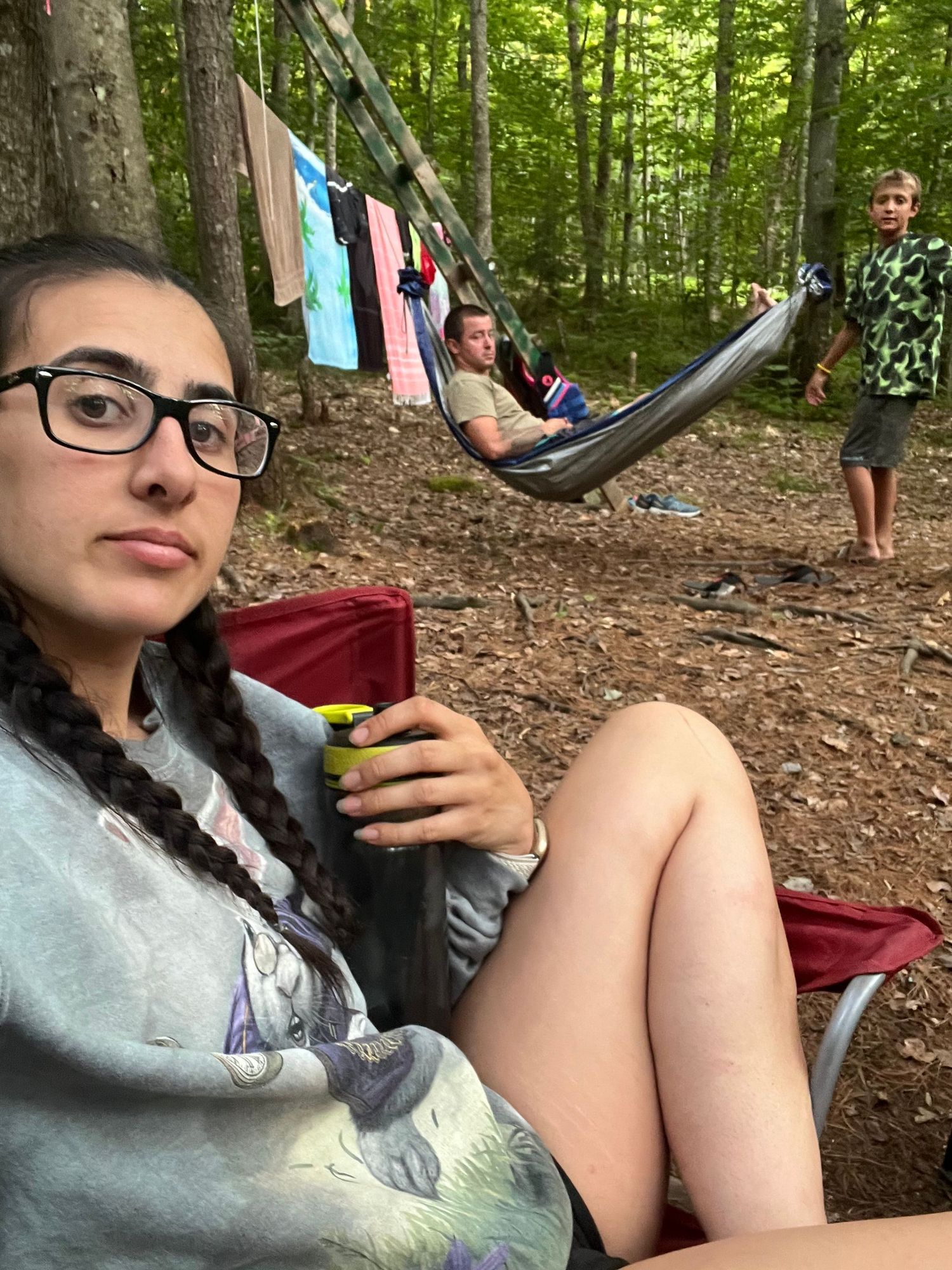 Peaceful campsite scene with hammock and clothesline strung between trees in forest.