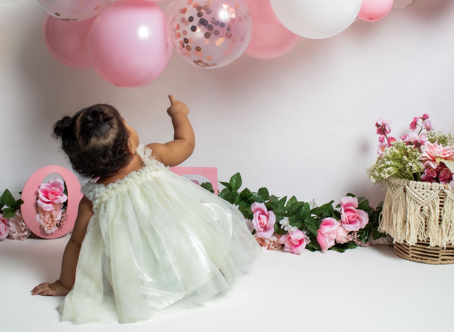 Child in mint green dress twirling among pink balloons and roses during photoshoot.