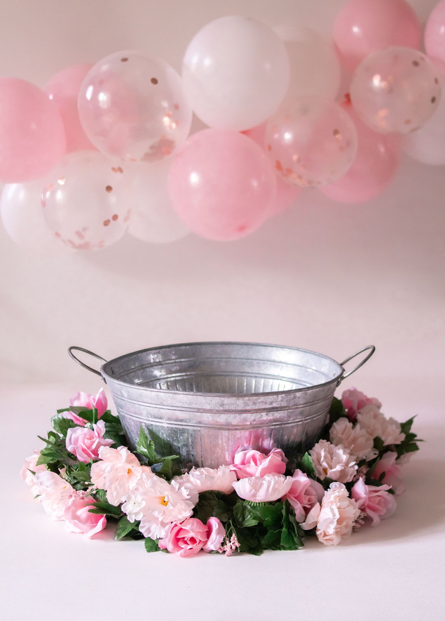 Pink and white balloons above a metal tub surrounded by pink floral decorations.