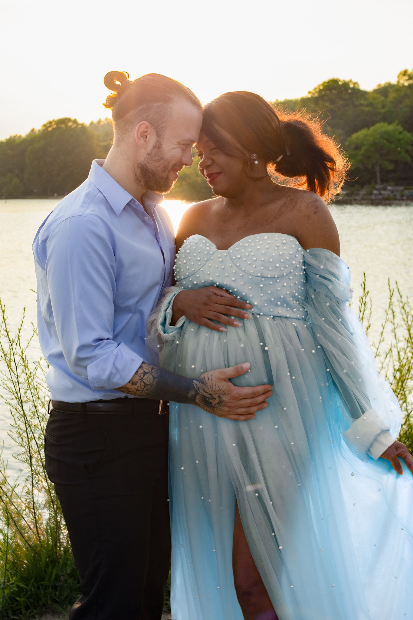 Romantic sunset maternity photo of couple in blue dress by waterfront.