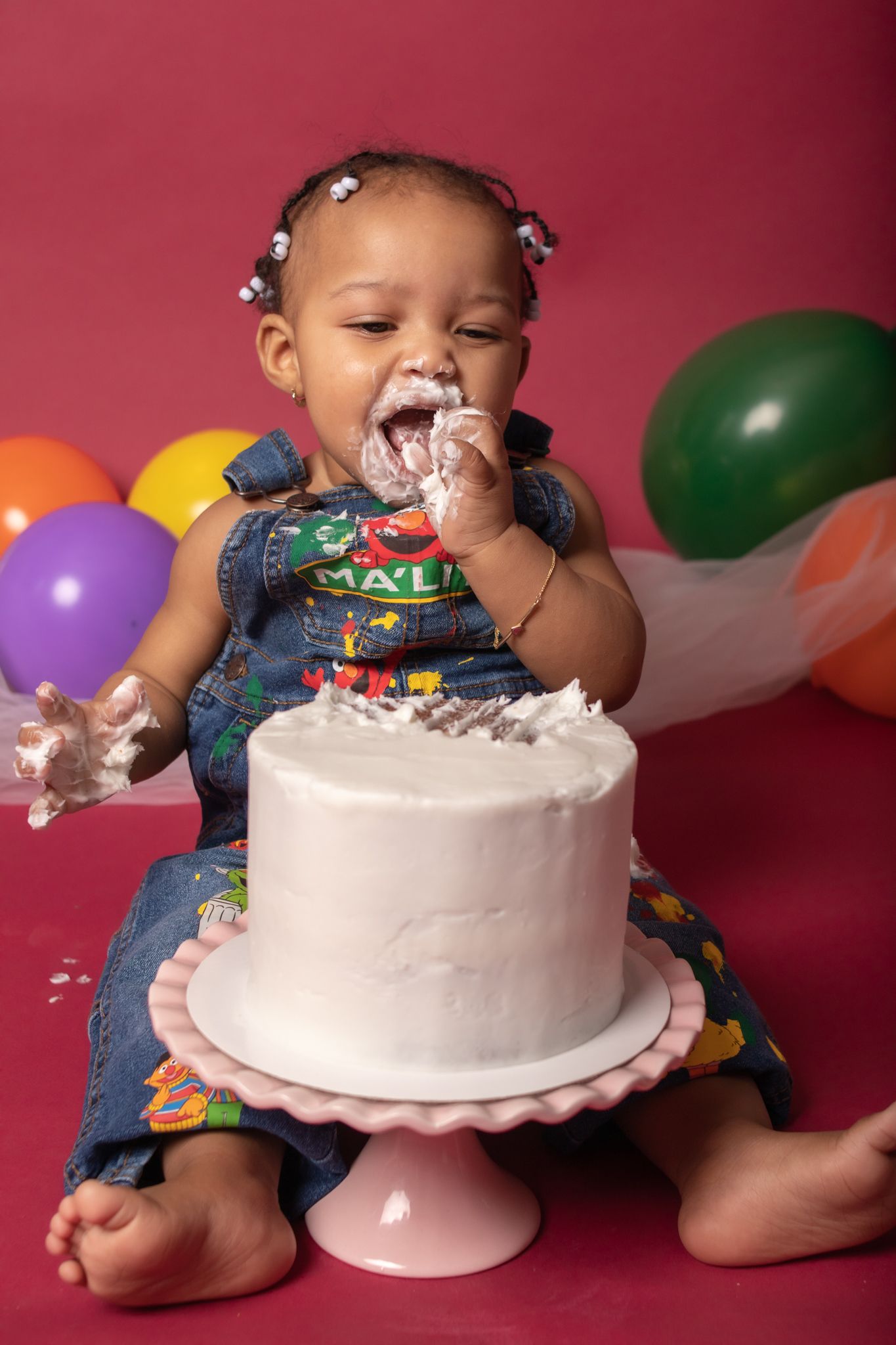 Birthday celebration with white cake and colorful balloons against burgundy backdrop.