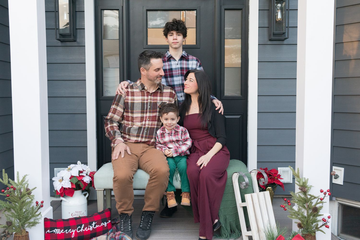 Holiday portrait on a front porch decorated with festive flowers and red wagon. Christmas Mini session