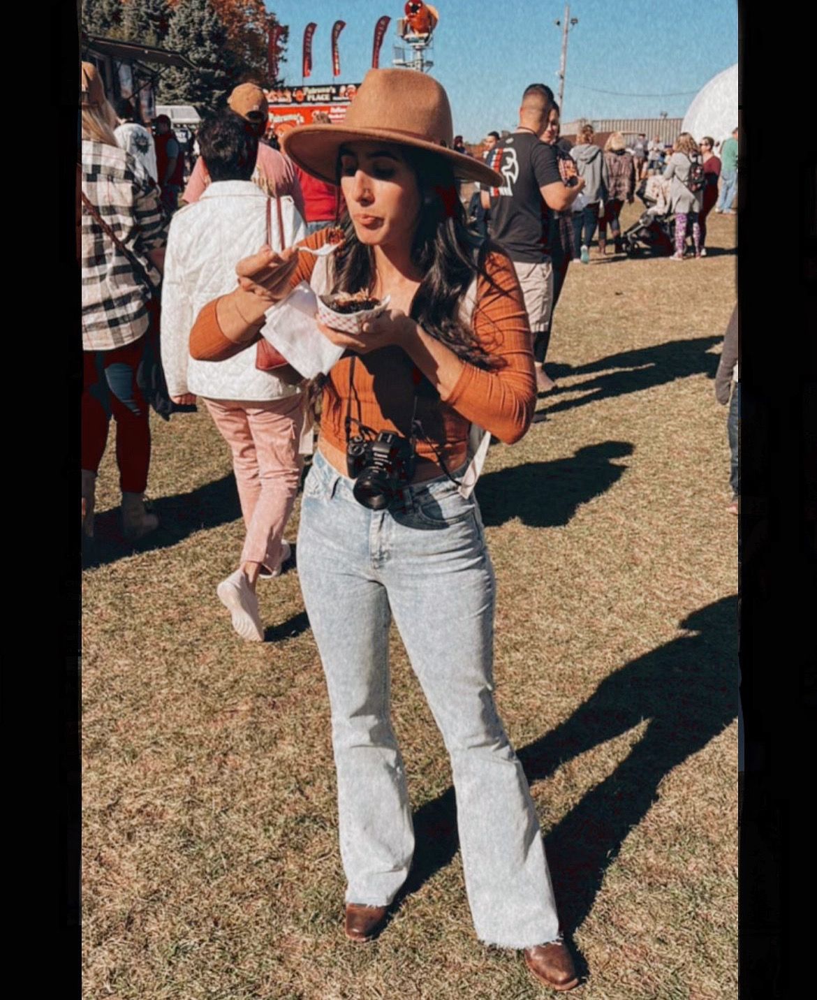 A festival-goer in a brown hat and jeans enjoys outdoor festivities.