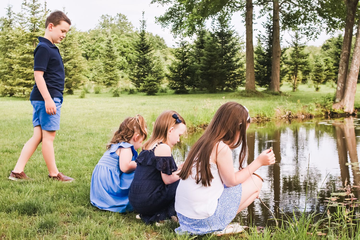 Children crouched by pond's edge exploring nature on summer day.