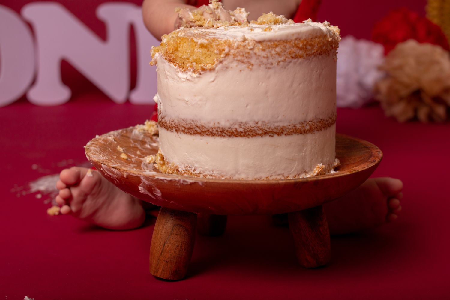 Elegant white cake with gold accents displayed on wooden stand against burgundy background.
