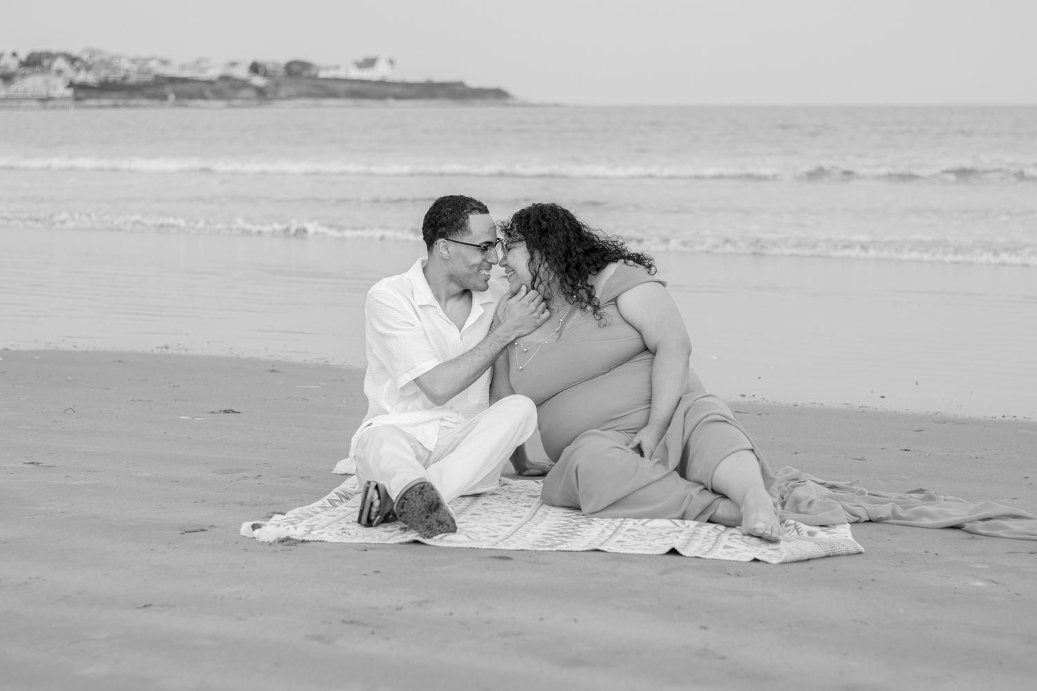 A romantic black and white beach scene with a couple sitting together on a blanket by the ocean.